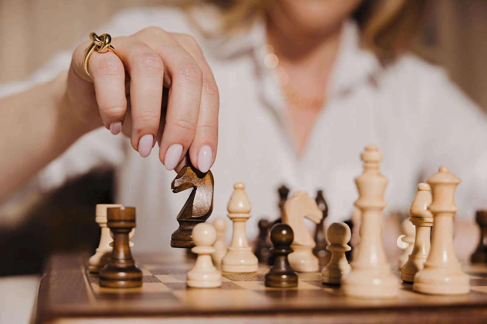 A woman makes a move in a game of chess, holding a black knight piece over a chessboard with wooden pieces.