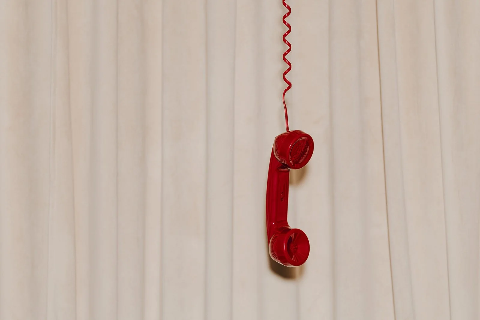 Red vintage telephone hanging on a beige wall.