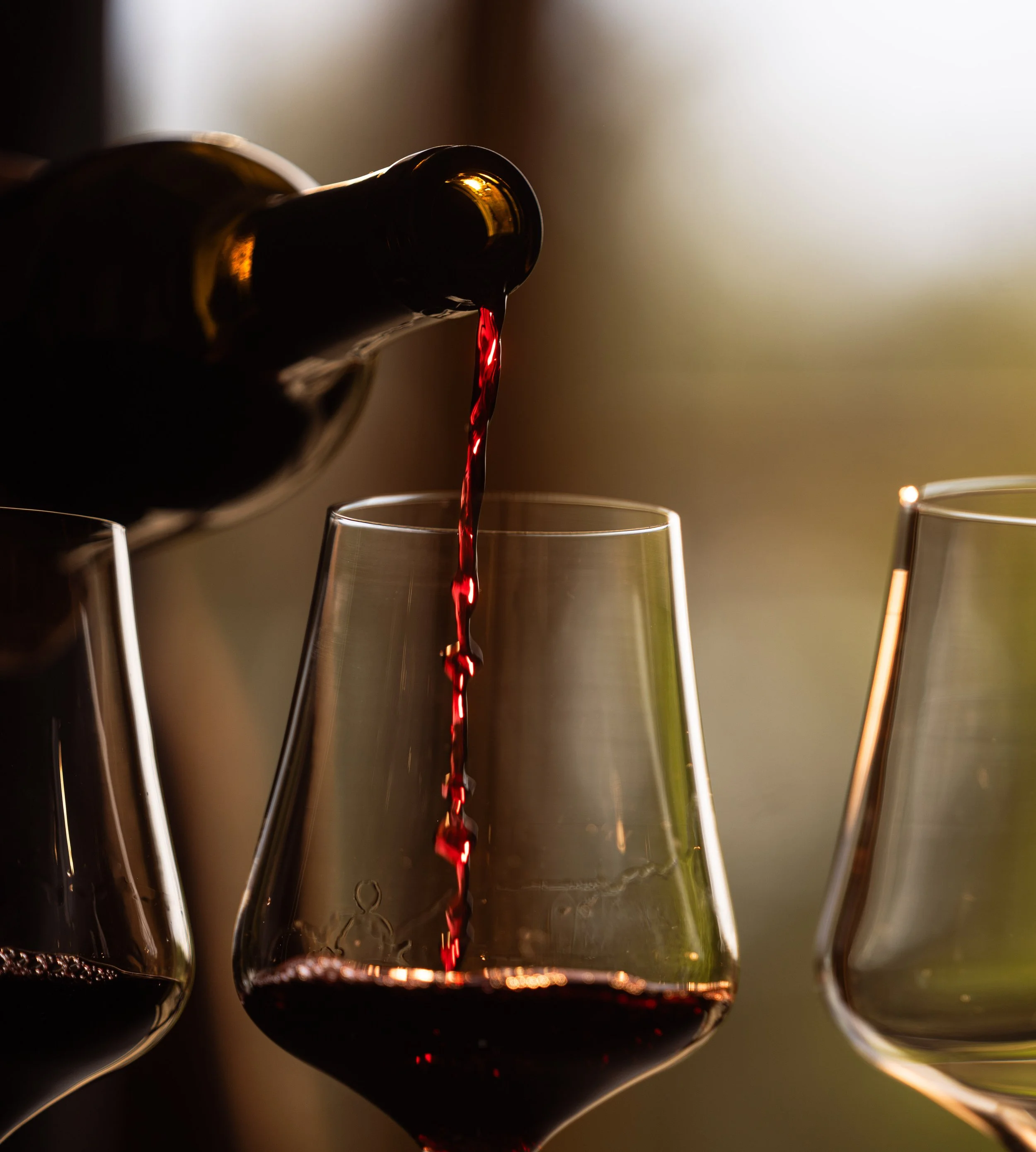 Close-up of red wine being poured into a glass from a bottle, with two additional glasses of wine nearby.