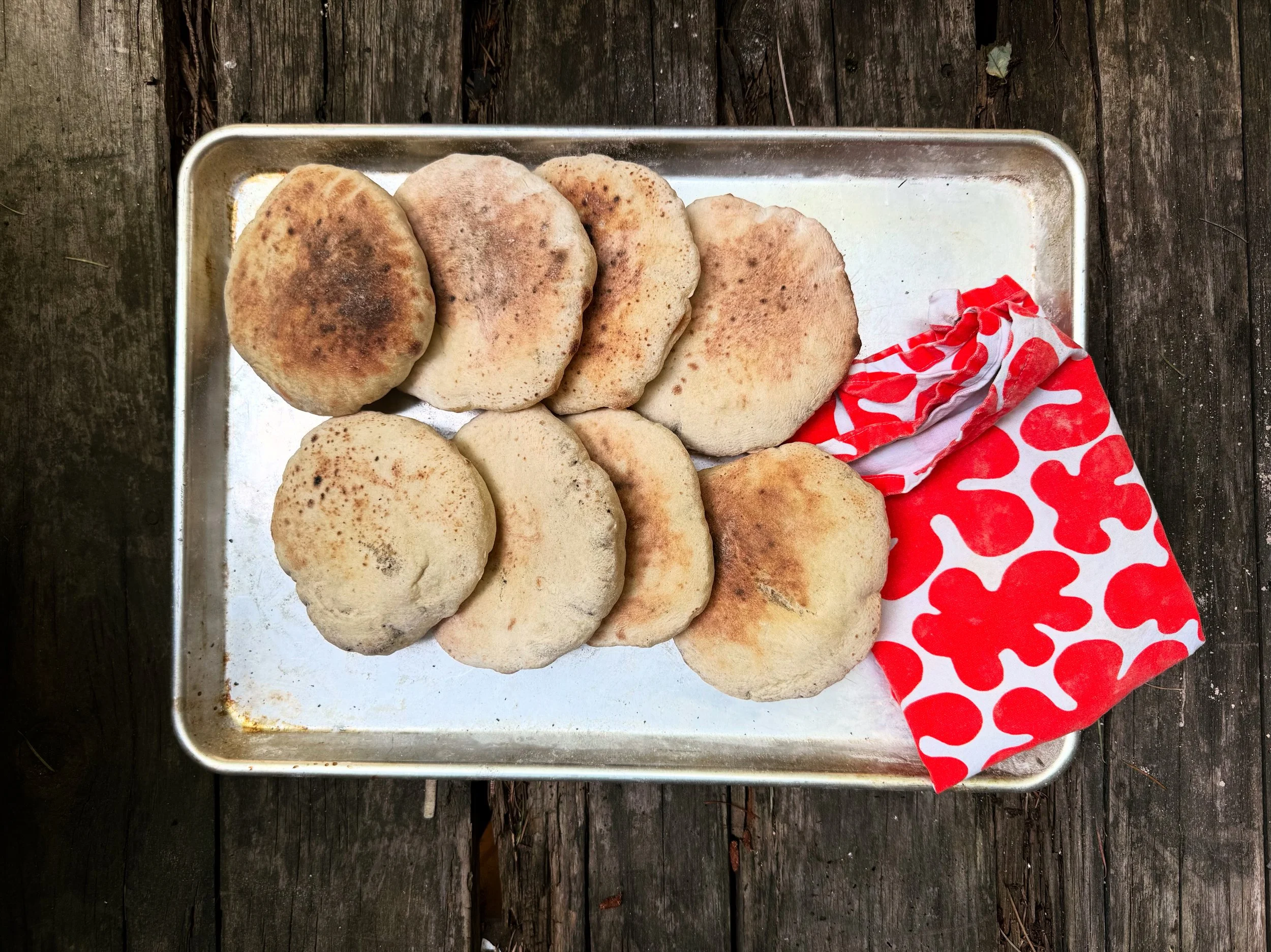 A metal tray with several pieces of flatbread on a wooden surface, partially wrapped in a red and white cloth.
