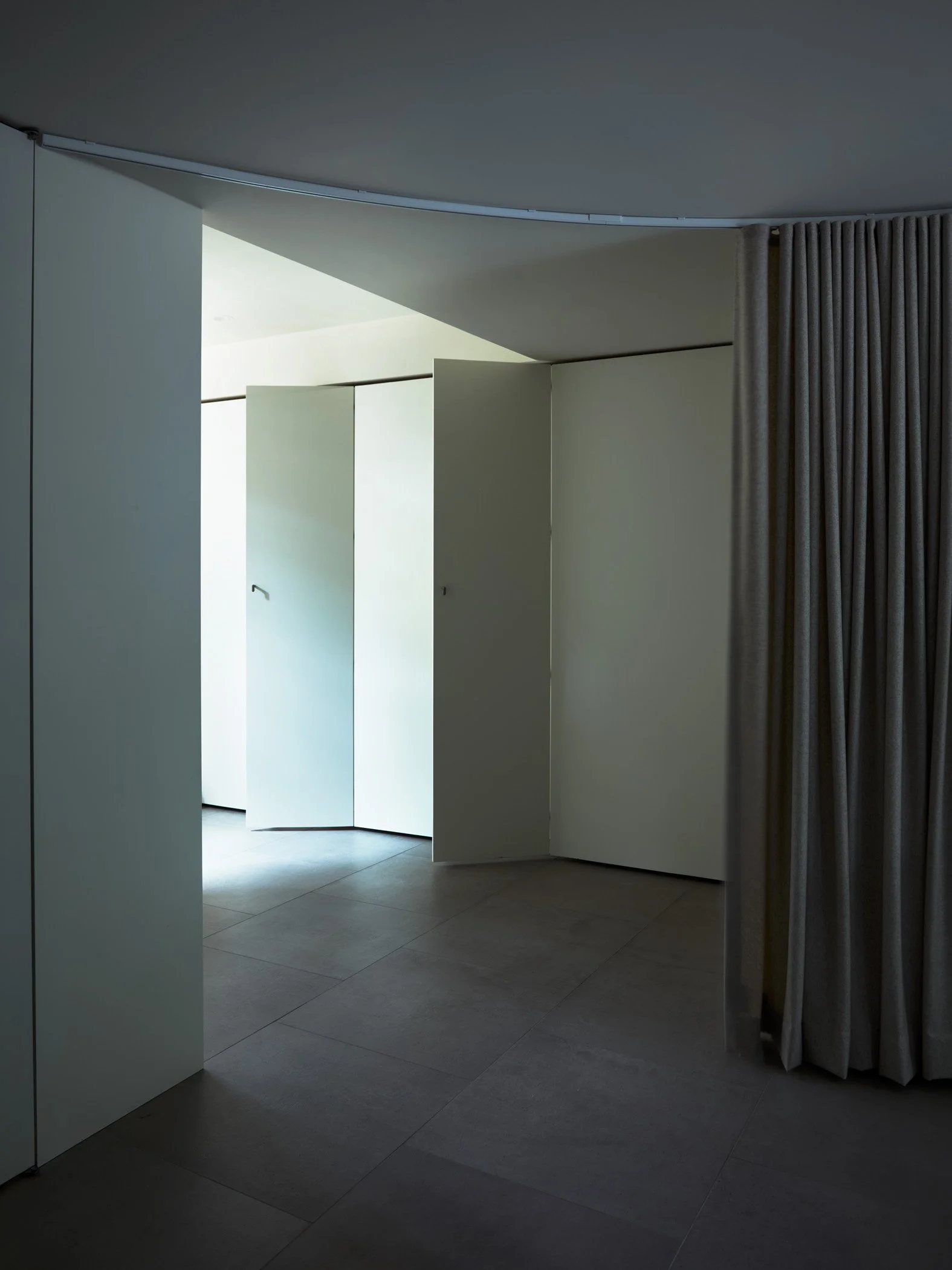 An interior space with a partially open sliding door, light-colored tiled flooring, white walls, a curtain on the right side, and natural light coming in from the outside.