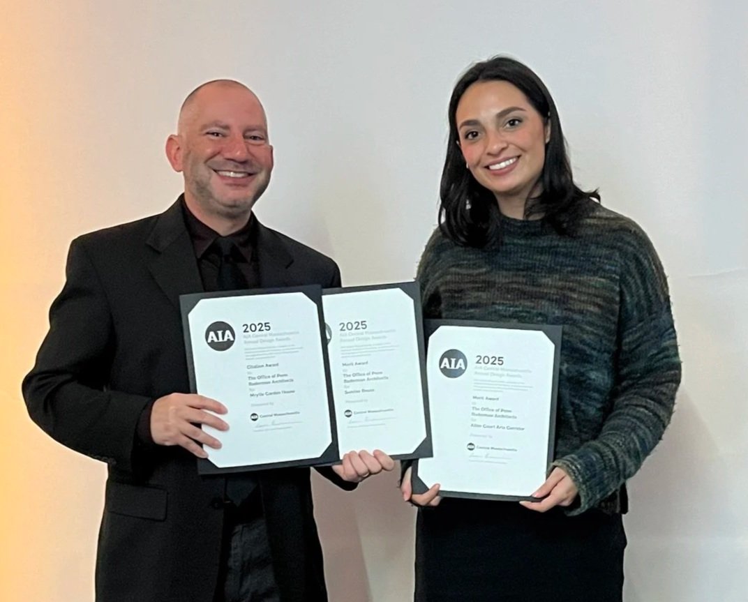 A man and woman smiling while holding awards and certificates at an architectural award ceremony.