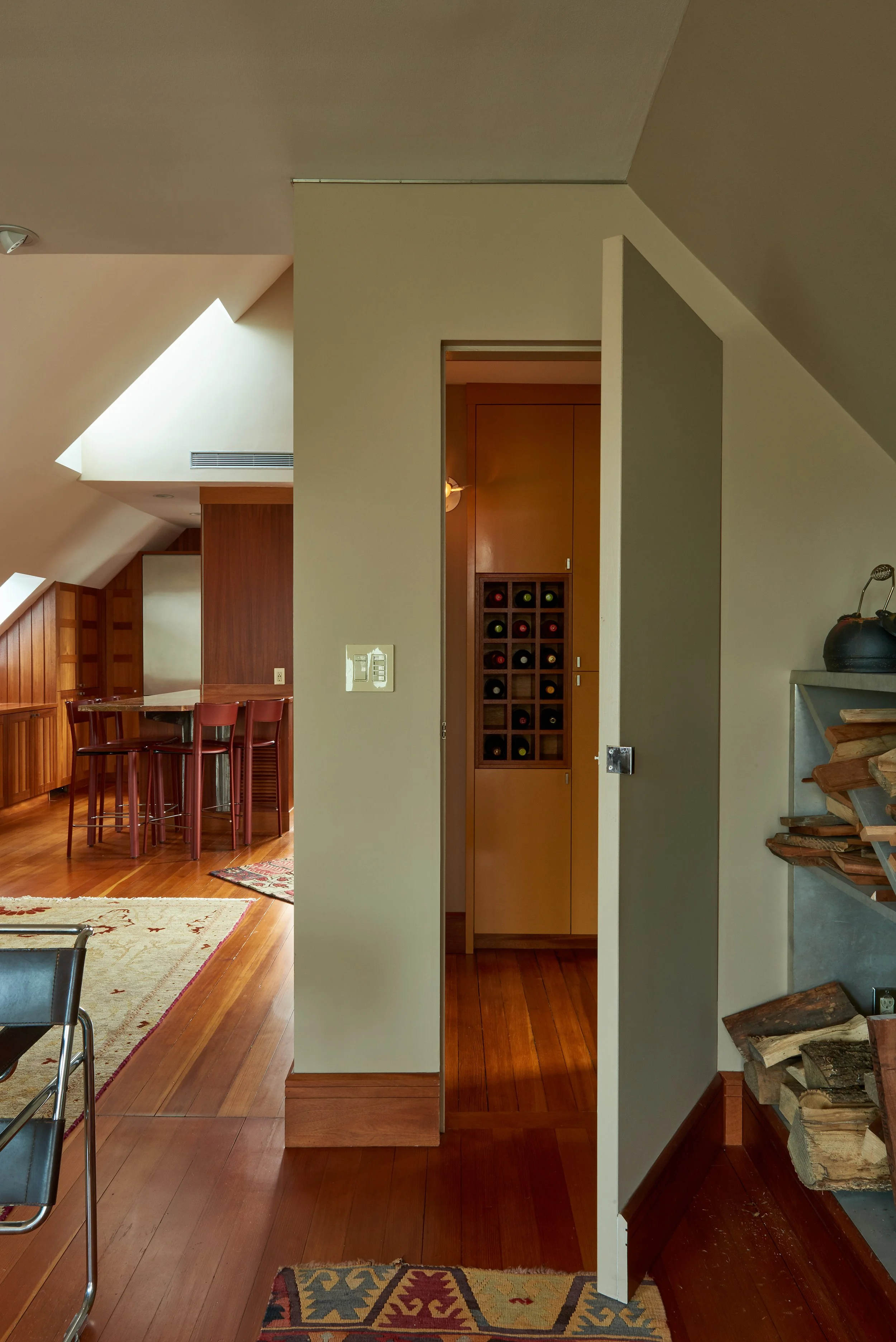 Interior view of a home with wooden floors, a staircase with logs on the side, and a wine rack built into a wood-paneled wall.