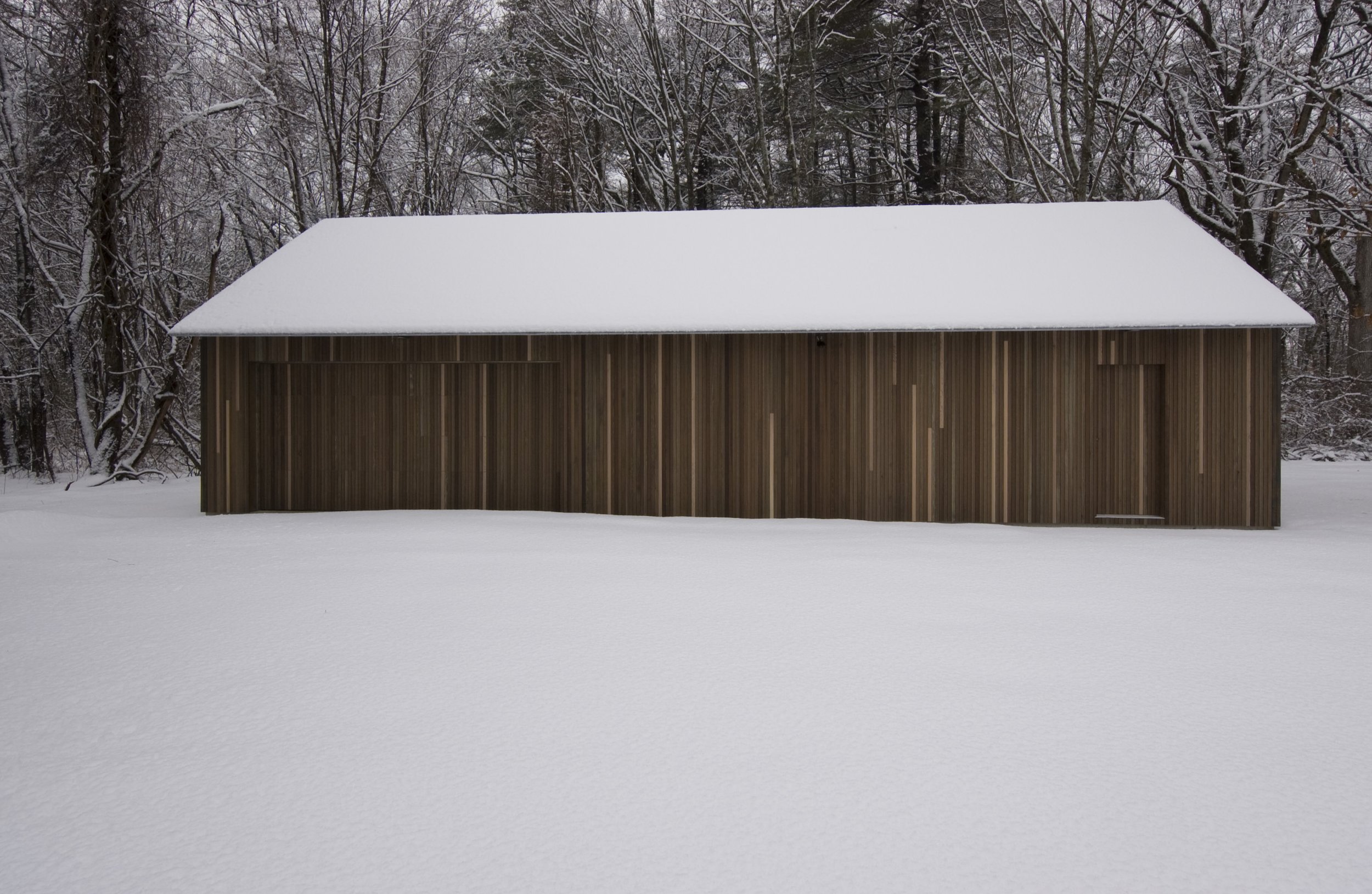 A snow-covered wooden building in a winter landscape surrounded by snow-covered trees.