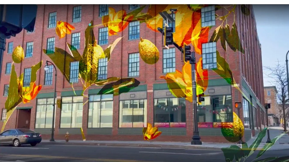 A building with large ground-floor windows and brick facade, overlaid with a colorful digital illustration of lemon tree branches with lemons and leaves, along with a city street scene including cars and a traffic light.