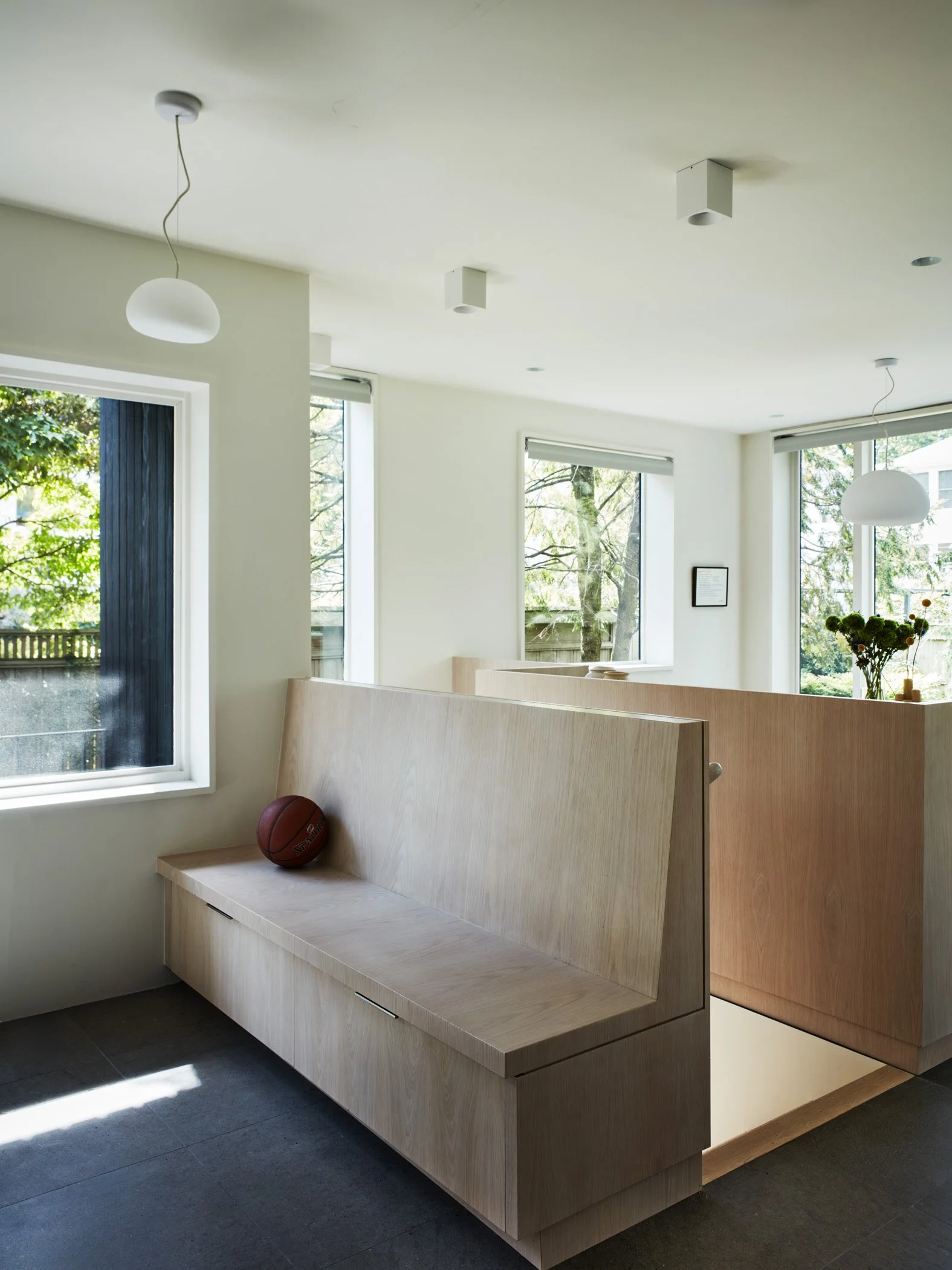 A modern interior with large windows, wooden partitions, and a basketball resting on a bench.