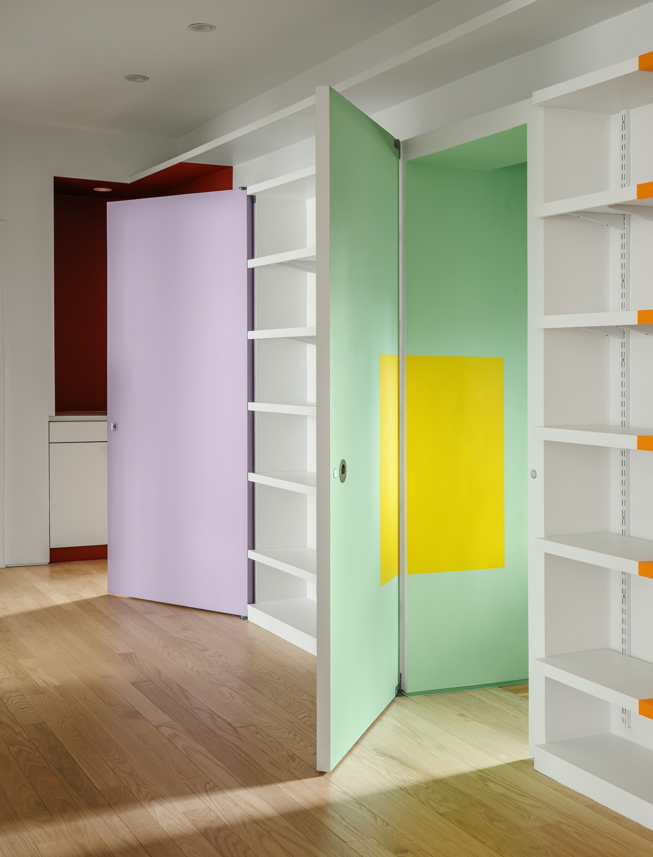 Empty white bookshelf with colored panels in purple, green, and yellow, set on a light wood floor.