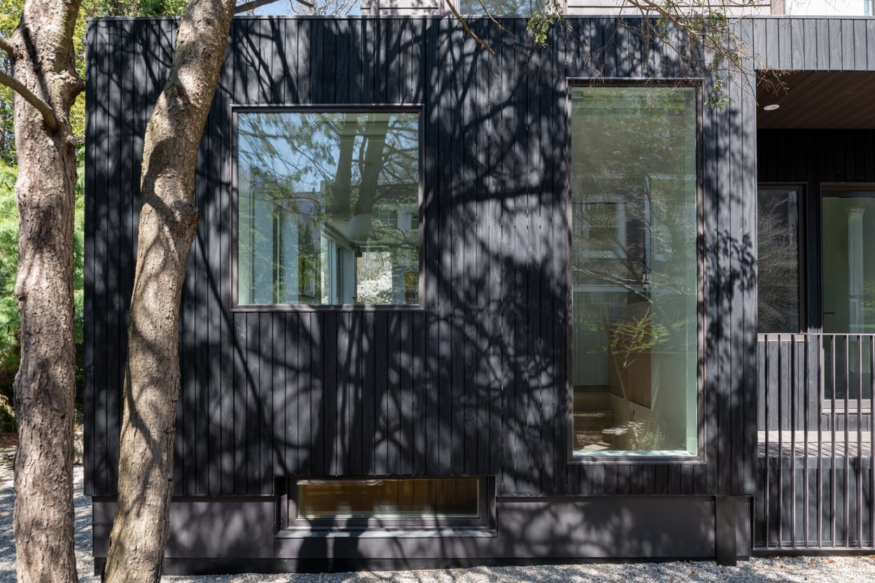 Modern black building with large windows, surrounded by trees casting shadows.