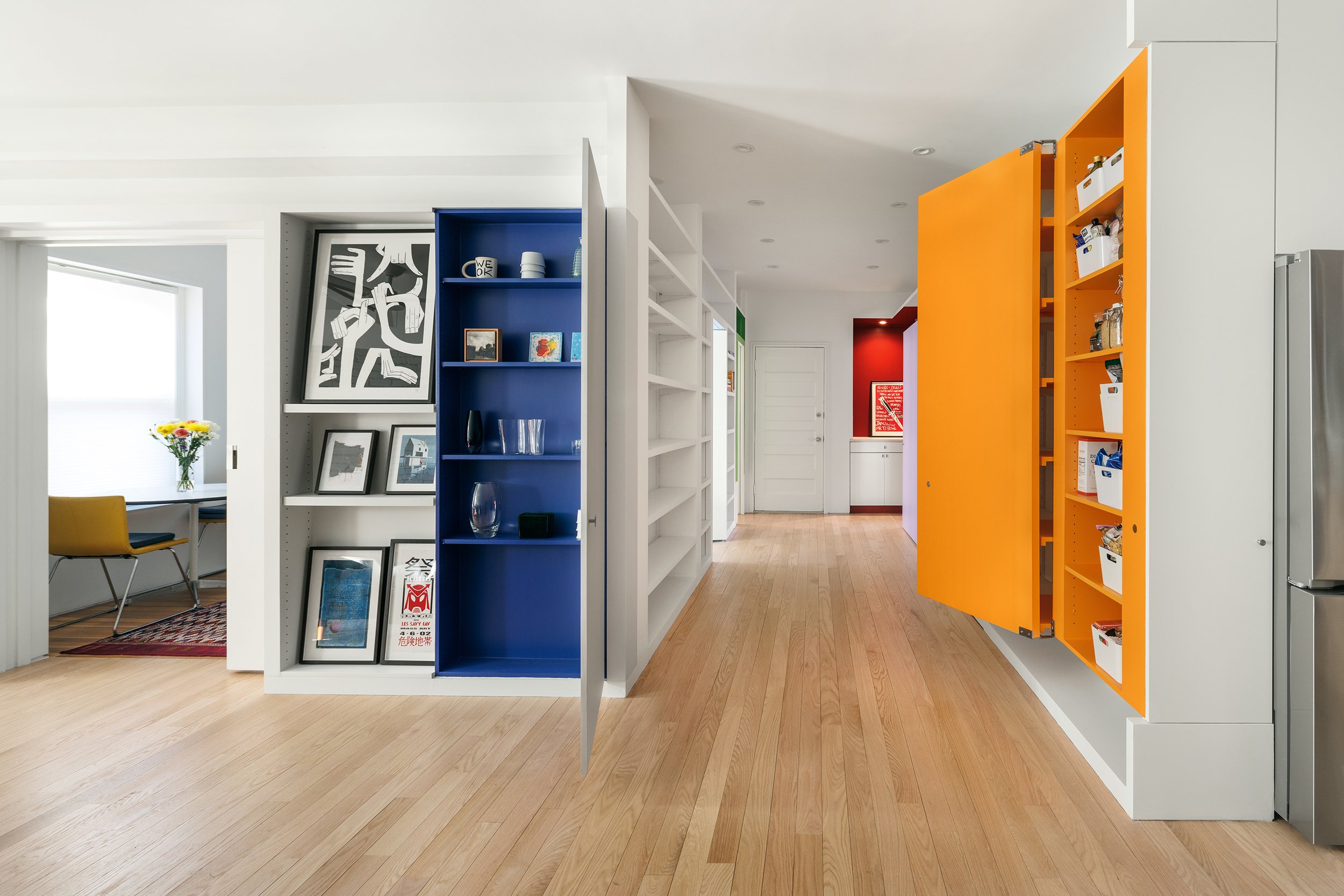 Interior of a home with colorful blocks, open shelving, and framed artwork. Light wooden flooring and white walls.