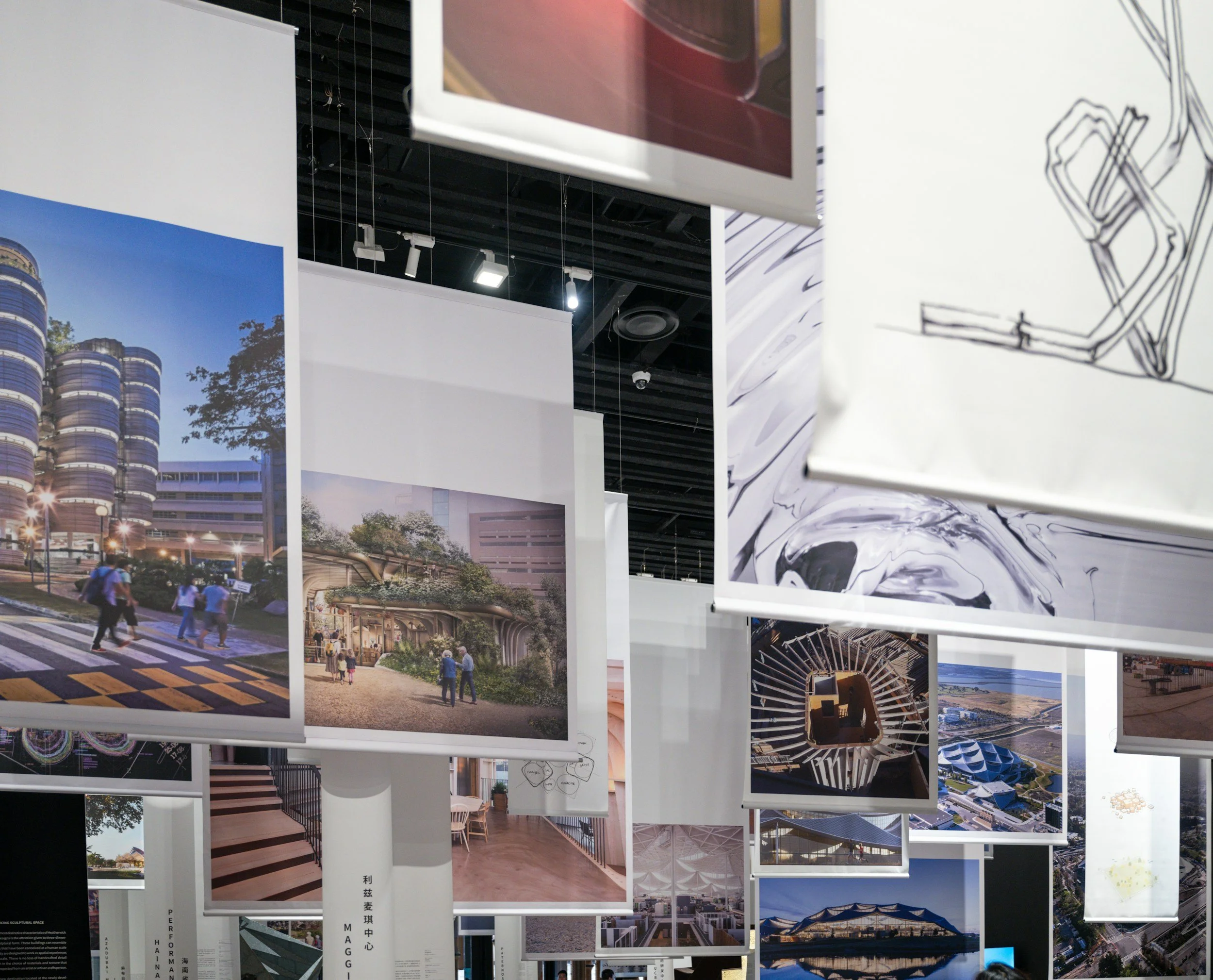 Multiple printed photographs and illustrations hanging on display, showcasing various architectural designs and urban landscapes, including buildings, parks, and cityscapes.