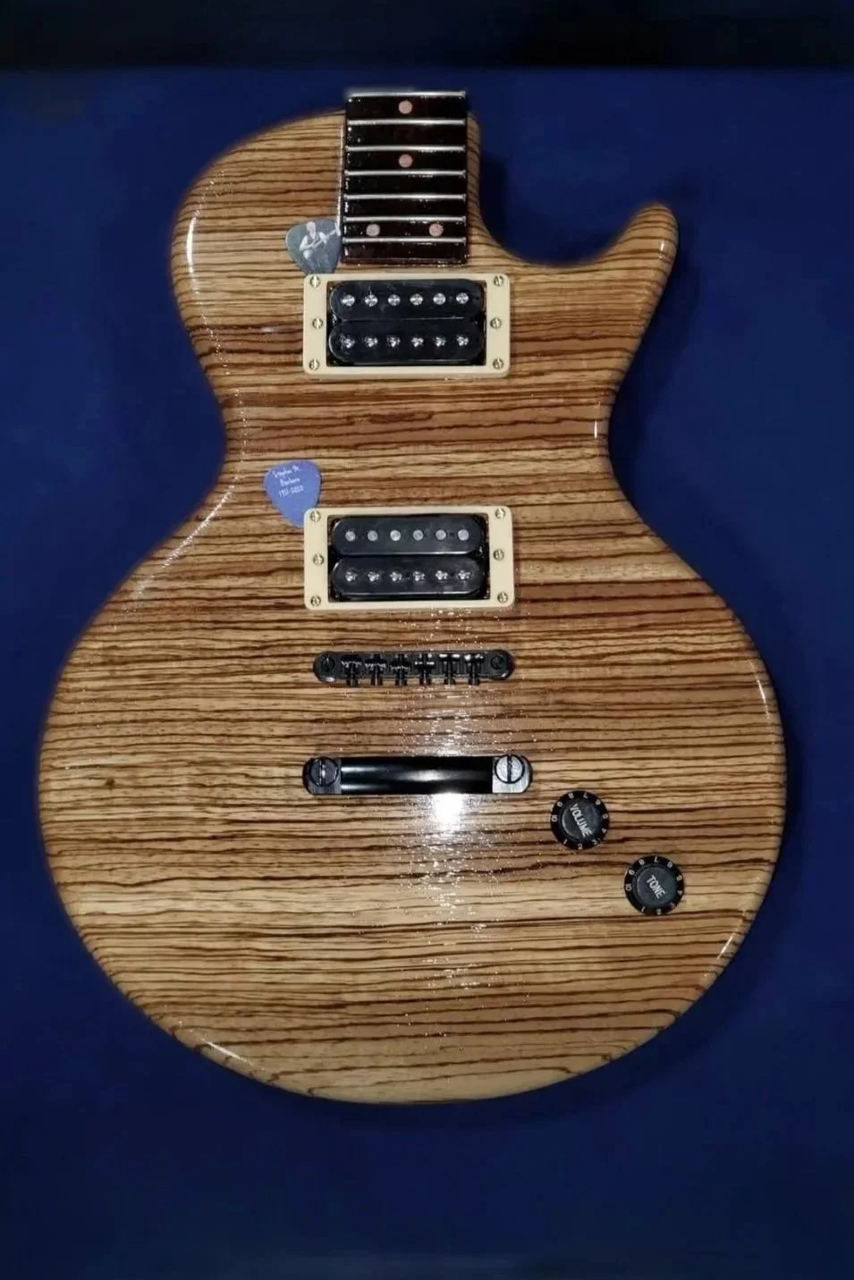 guitar urn with a wood grain body, two humbucker pickups, one volume knob, one tone knob, and a bridge, set against a dark blue background.