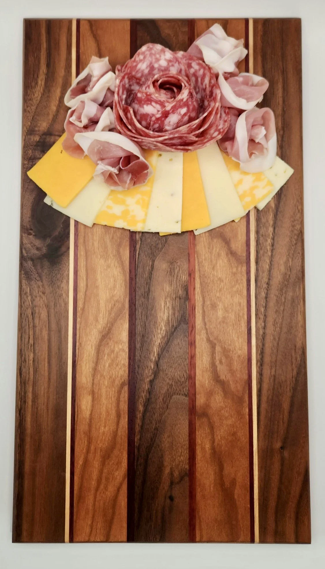 Charcuterie board with sliced cheese, salami, and prosciutto on a wooden serving board.
