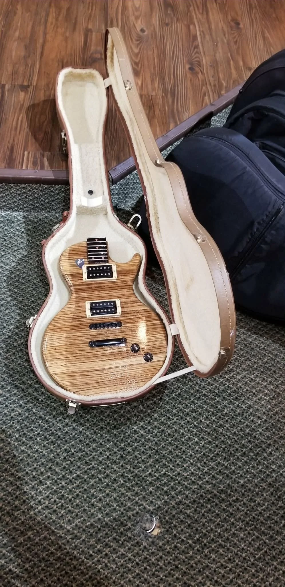 A guitar urn with a wood grain finish inside an open hard shell guitar case