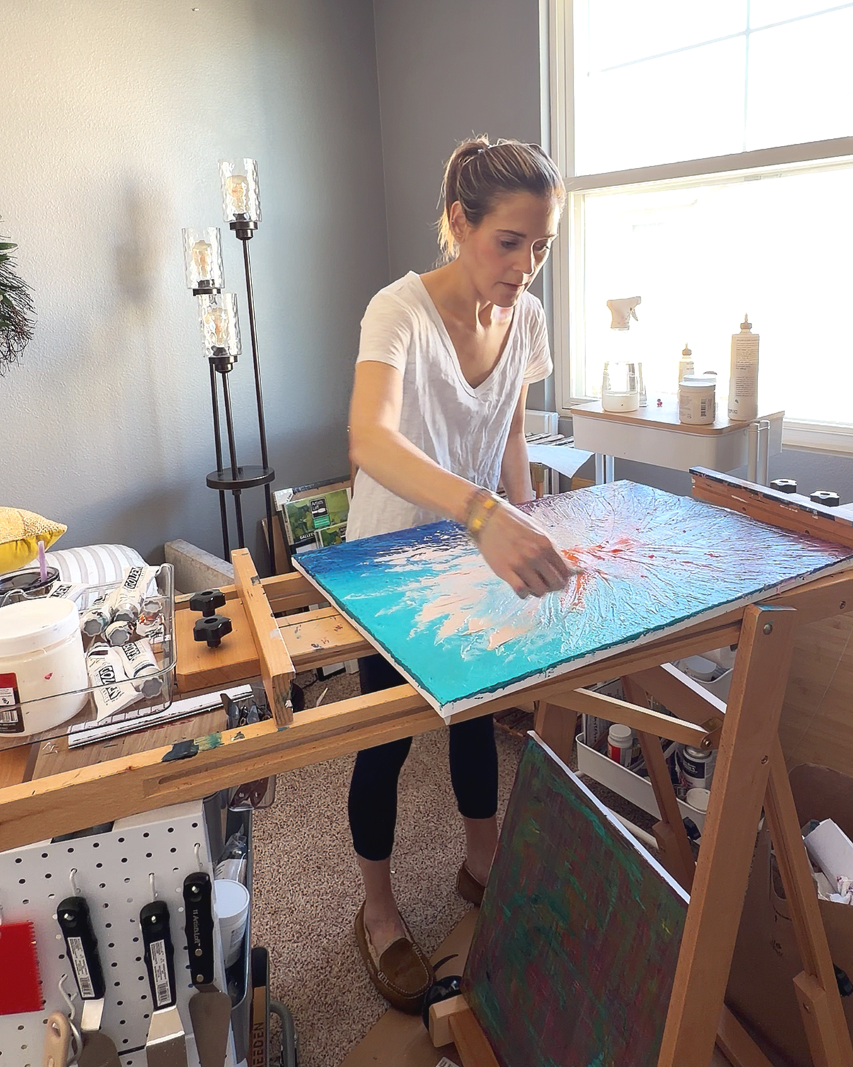 Lisa Bassett, founding artist of LBW Creative Studio creating an original abstract impasto painting on a canvas in a bright art studio.