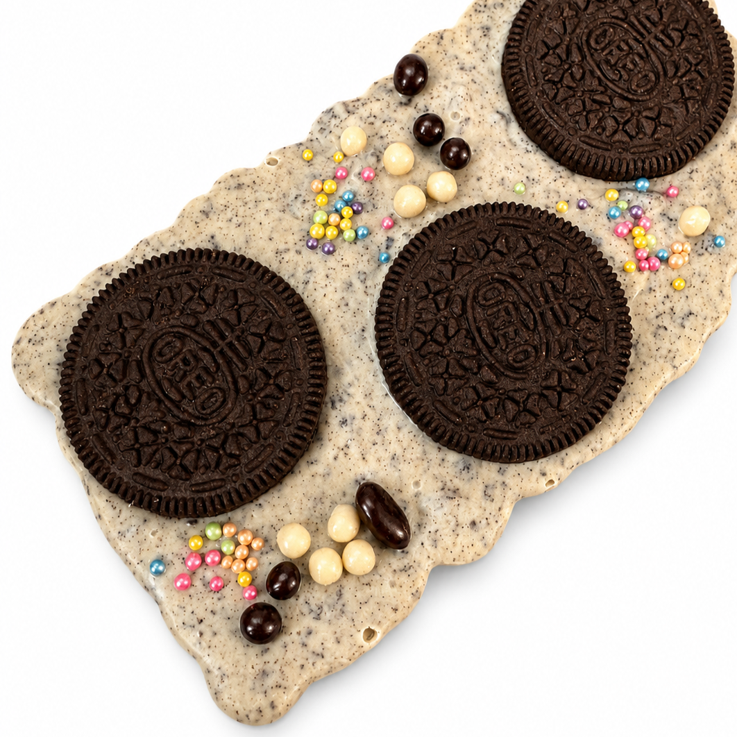 Large Belgian white chocolate bark with crushed oreo cookies topped with three full  oreo cookies, colourful sprinkles, dark chocolate-covered cacao nibs and white chocolate covered crisp balls