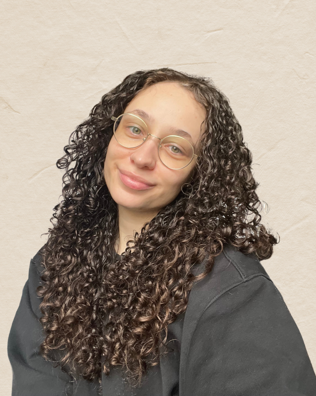 Portrait of a smiling woman with long curly dark hair and round glasses wearing a black shirt