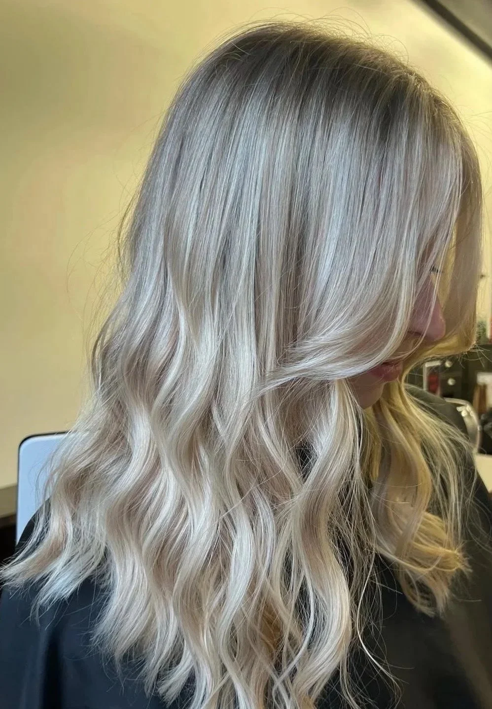 Close-up of a woman with long, wavy, blonde hair, sitting in a salon chair.