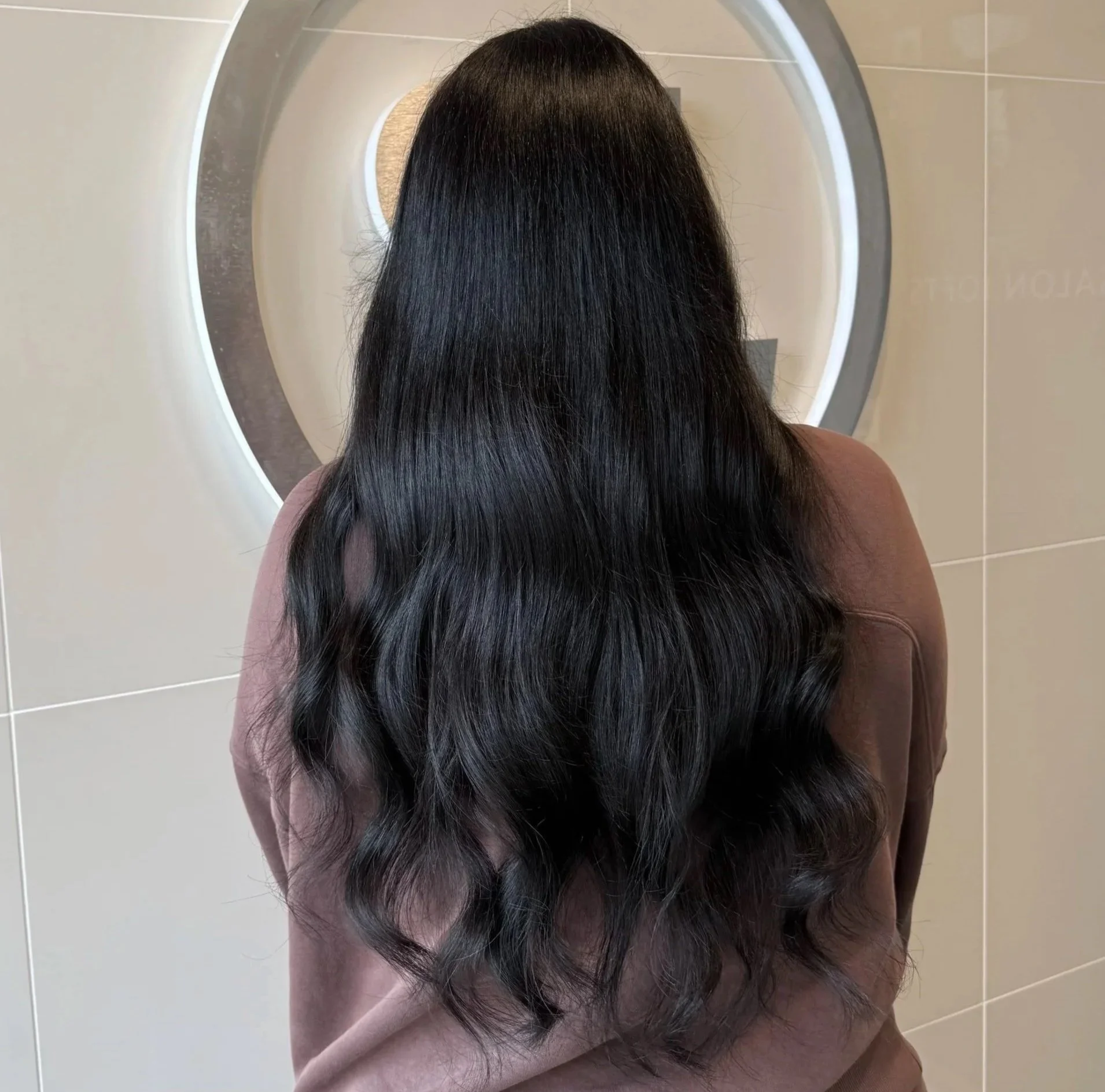Person with long, shiny black hair sitting in front of a round mirror.