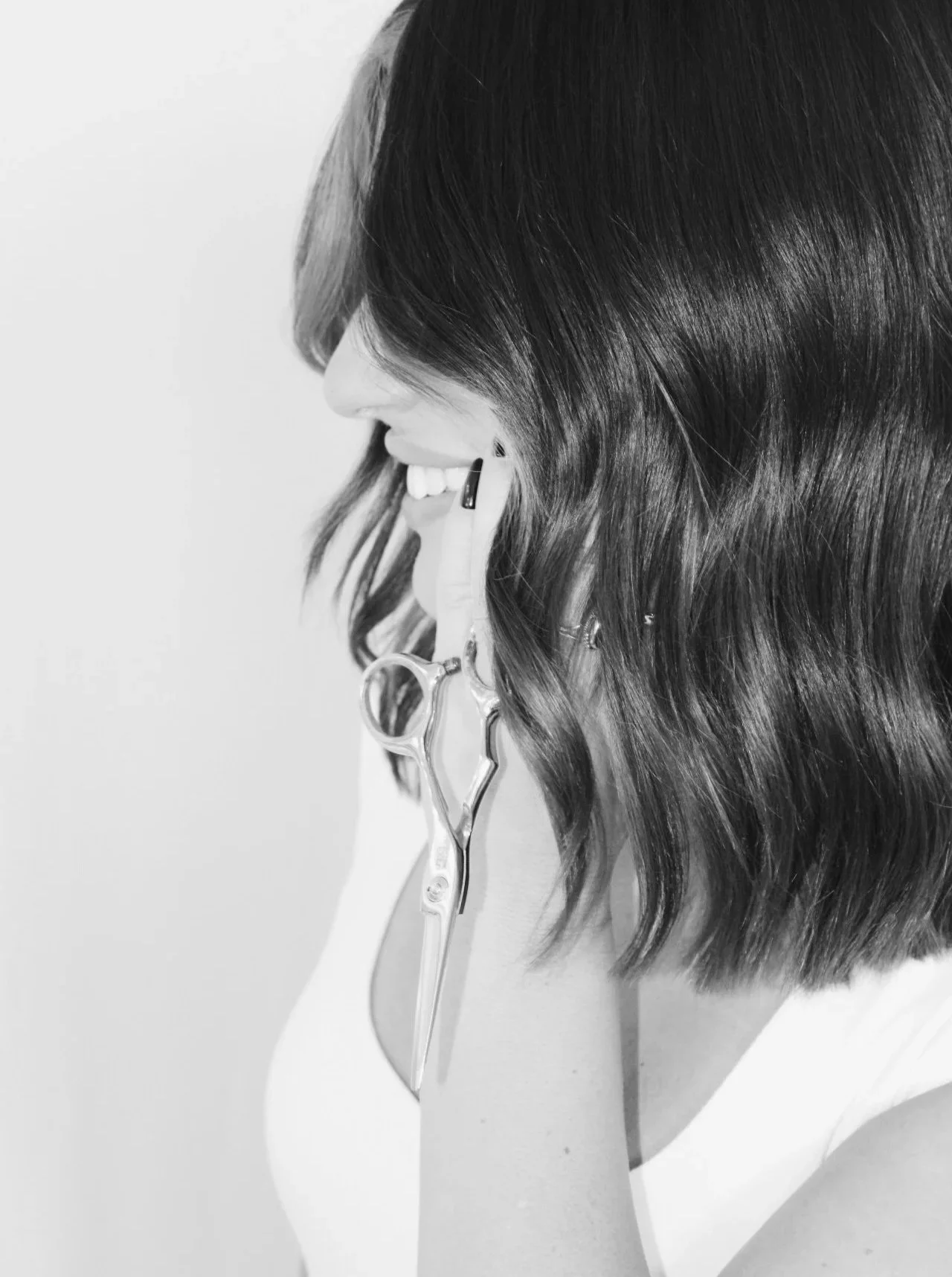 A woman with wavy hair talking on a cordless phone with a smile, seen in profile in black and white.