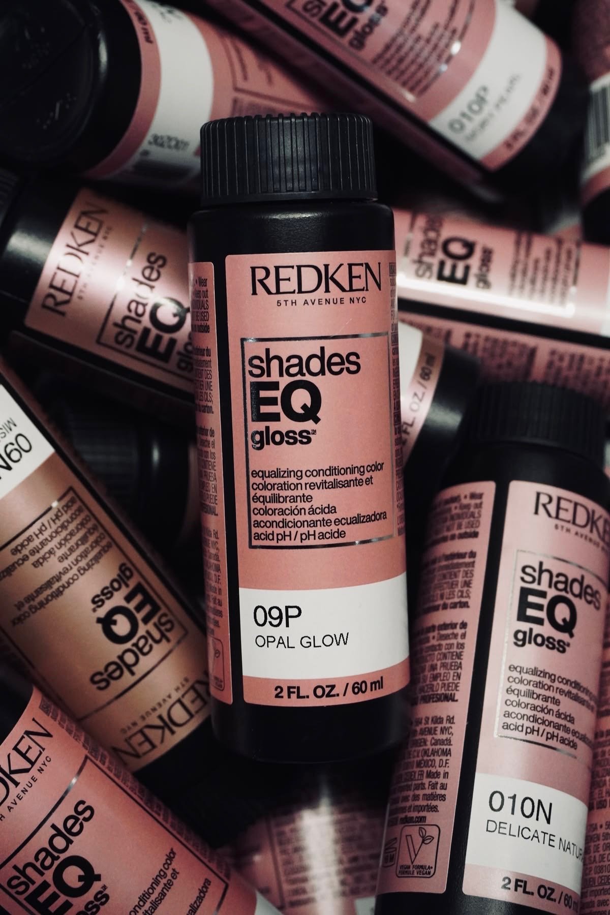 Several bottles of Redken Shades EQ gloss hair color, in the shade Opal Glow, surrounded by other bottles of the same product.