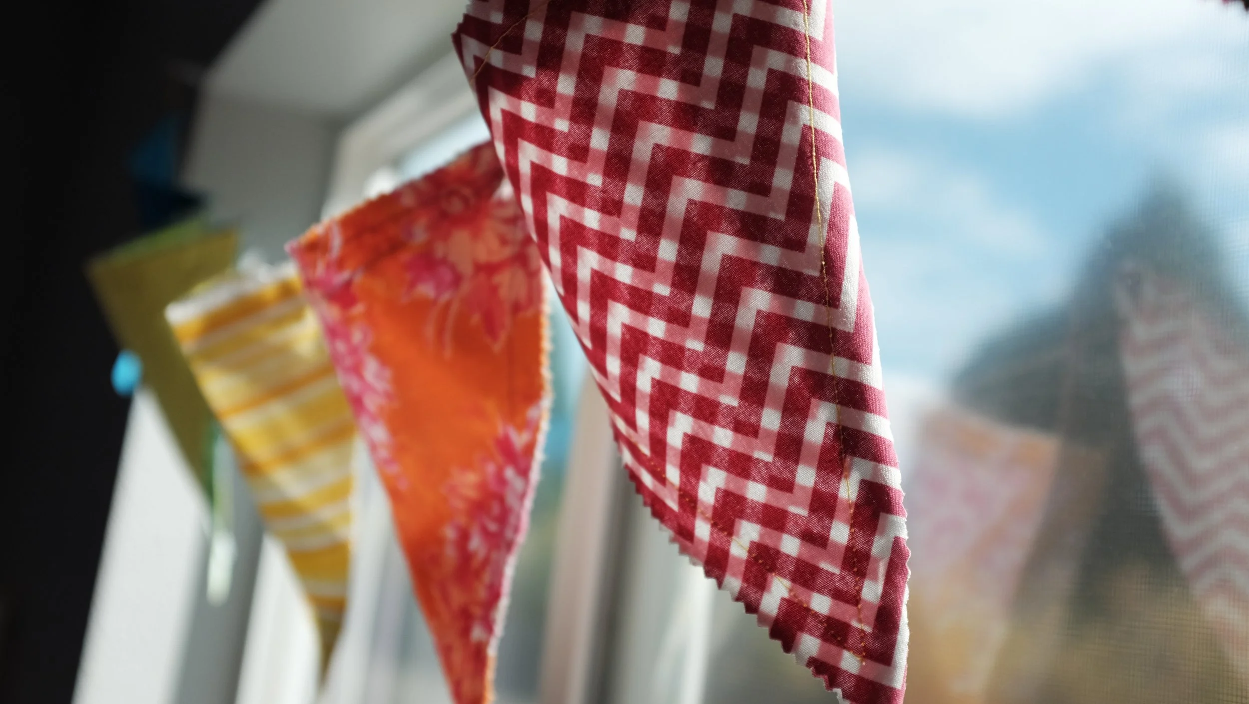 Close-up of colorful patterned cloths hanging on a line, with a window and blurry outdoor view in the background.