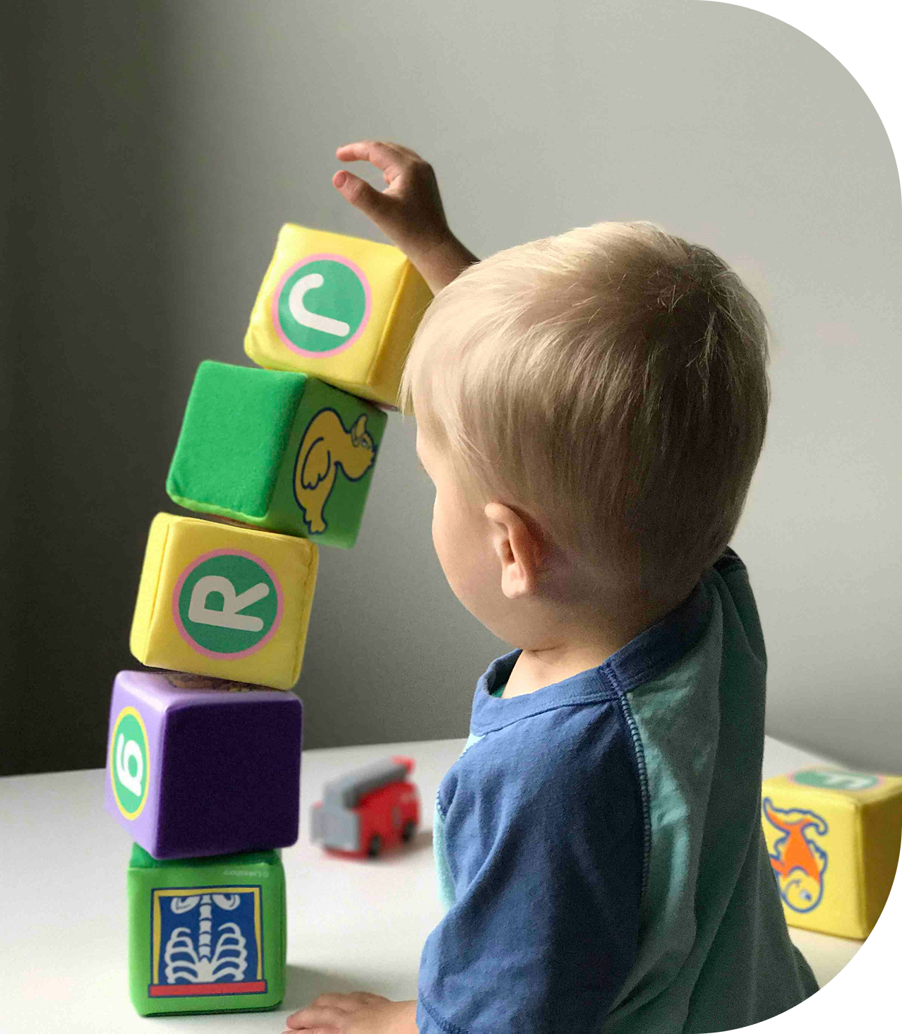 A young boy stacking colorful foam blocks with letters and animal pictures on them, as he plays at a table.