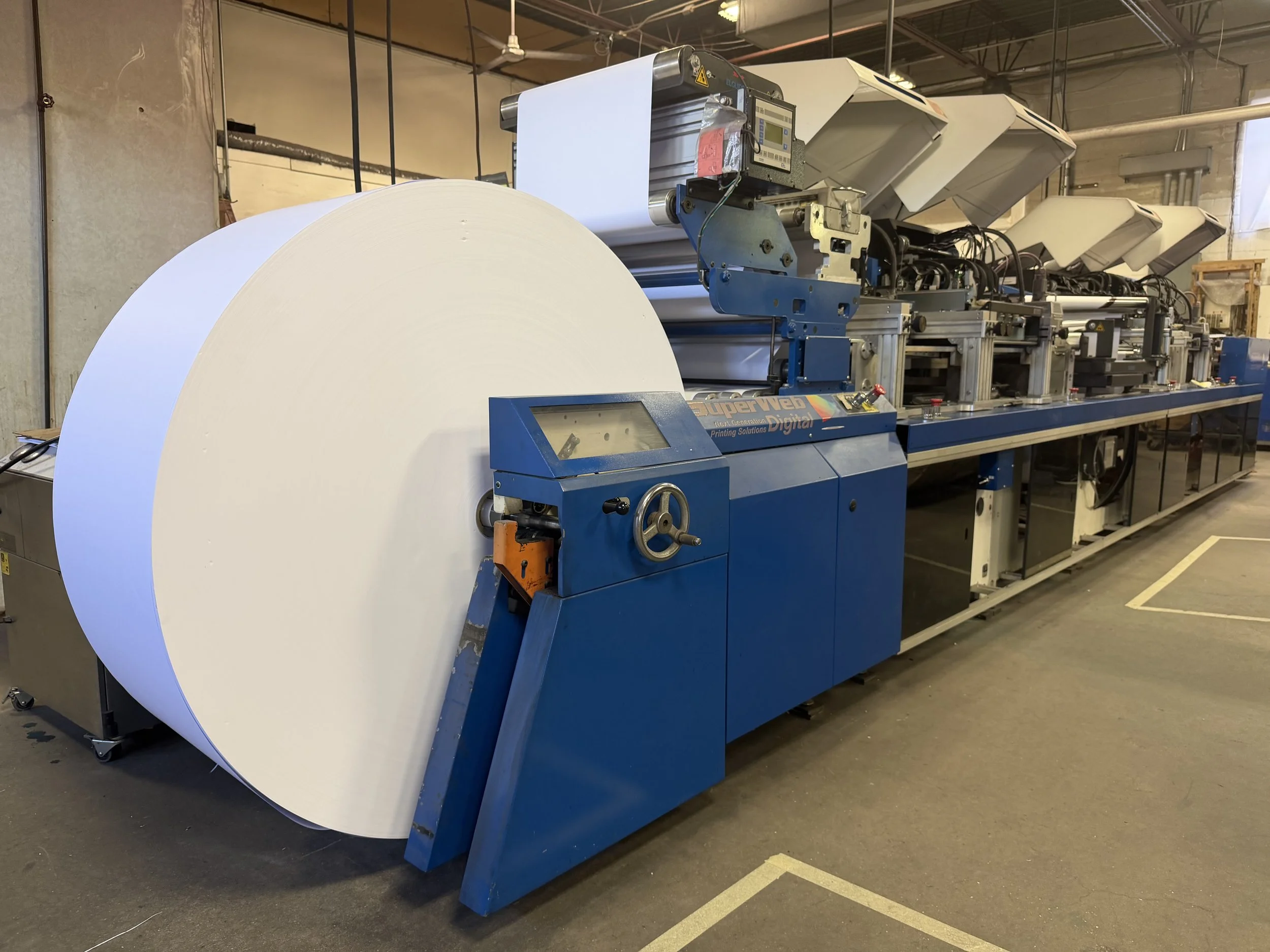 Industrial machine printing large sheets of white paper in factory setting.