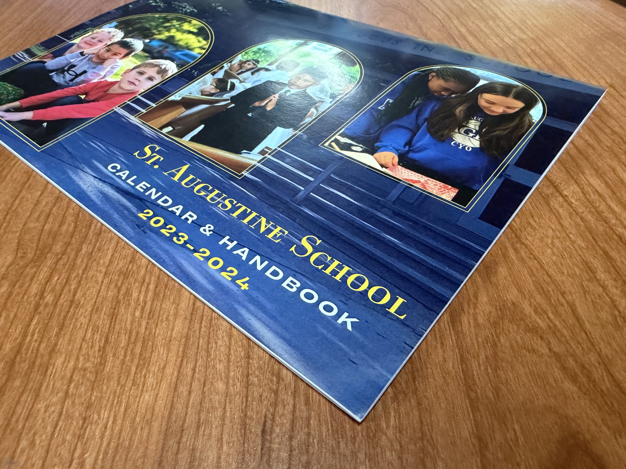 A printed calendar or brochure featuring photographs calendar year 2023-2024, placed on a wooden surface.