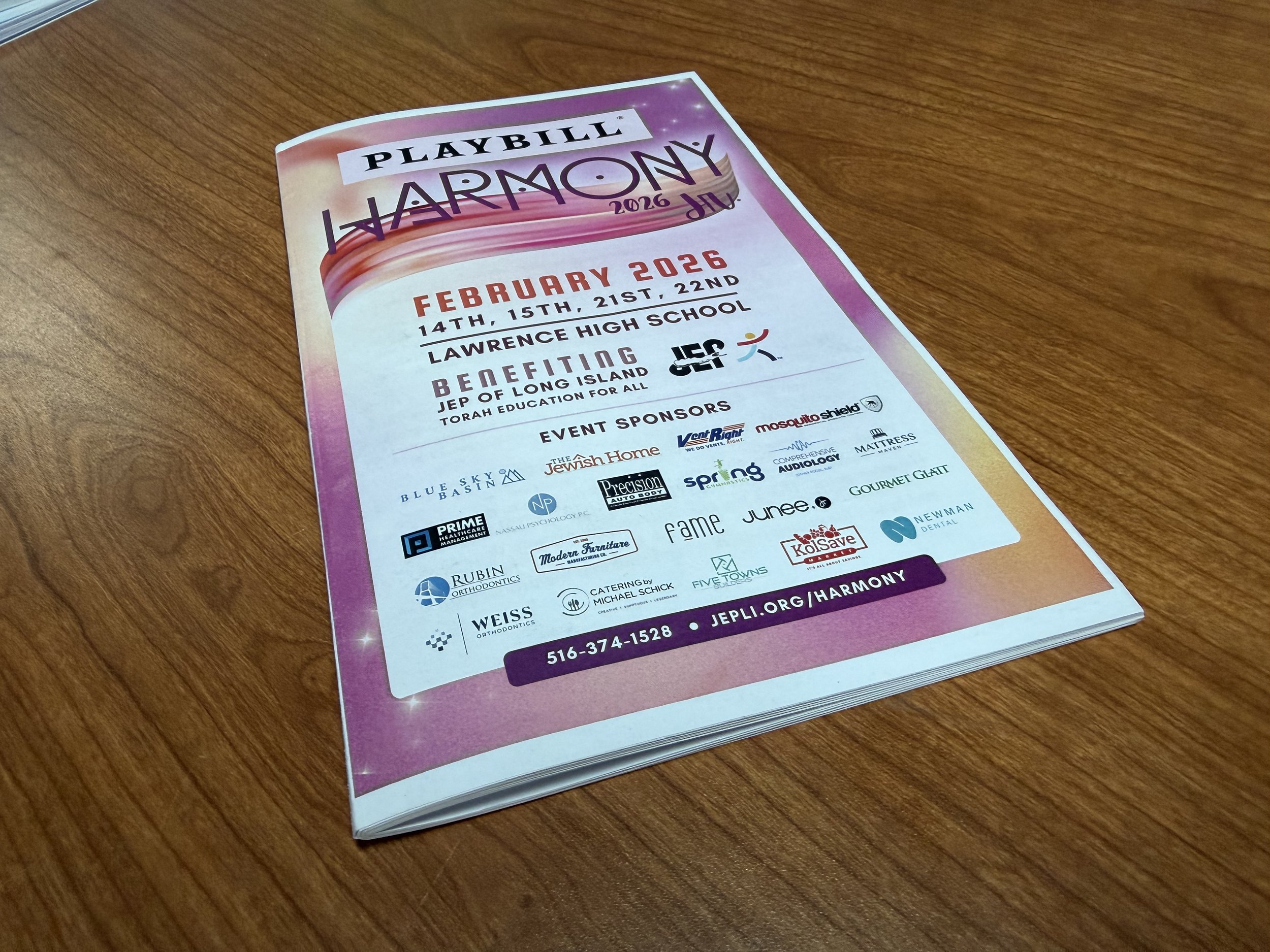 A brochure on a wooden surface promoting a charity event with various sponsor logos at the bottom.