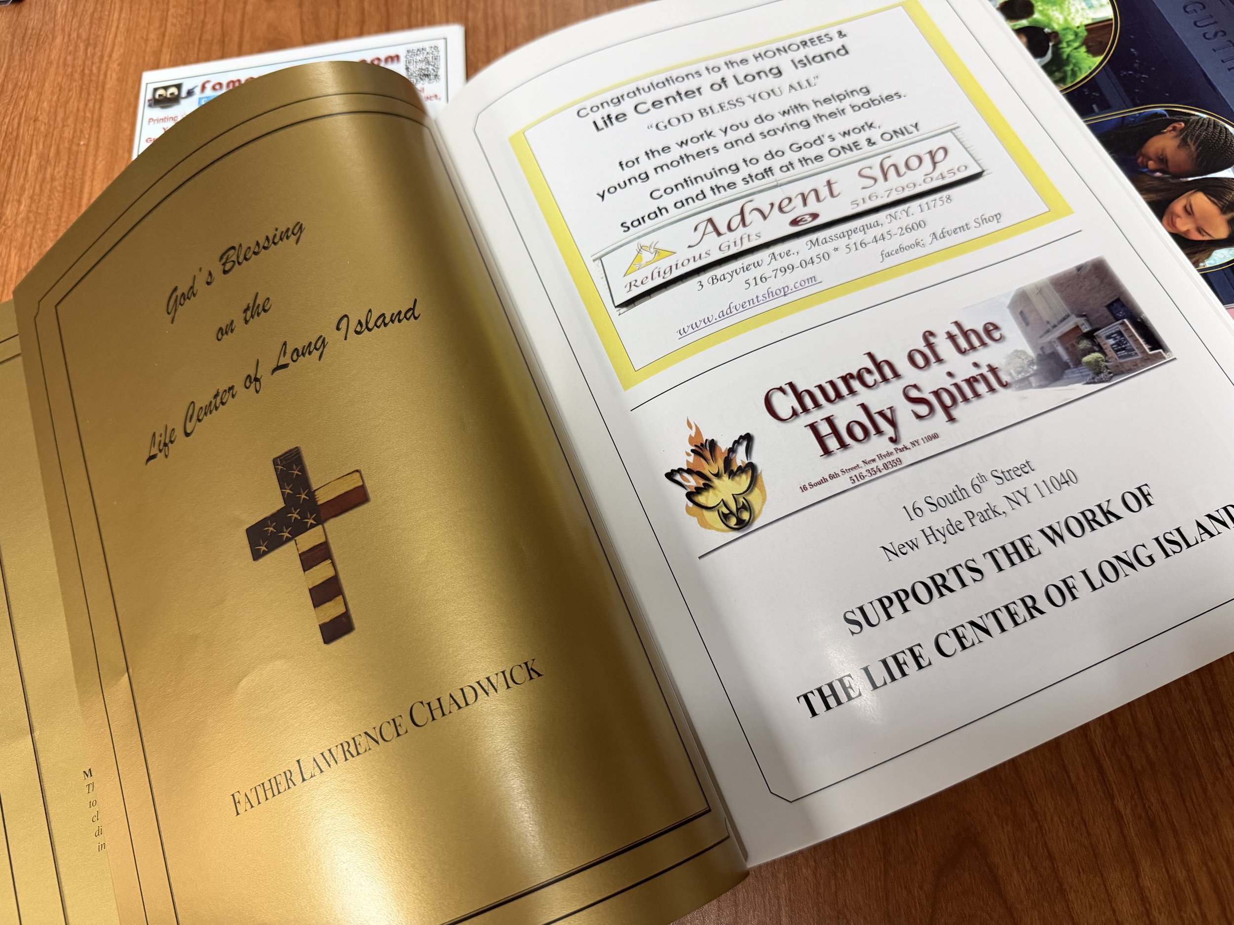 Open magazine with religious content and advertisements, featuring a gold-colored page with a cross and a white page with a congratulatory message, including contact information and advertisements for a religious gift shop and church.