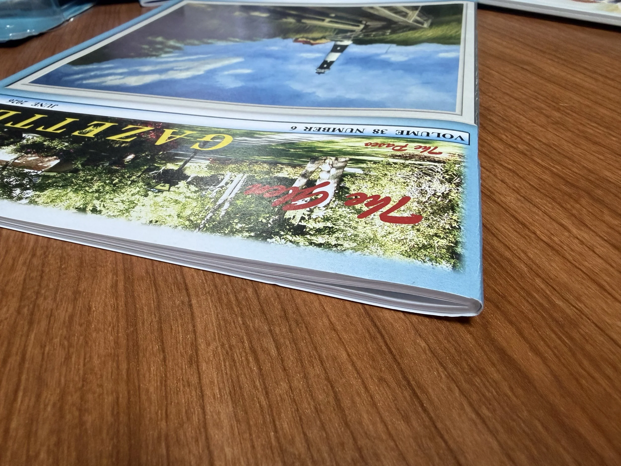 Close-up of a colorful brochure or magazine featuring a landscape with trees, a lake, and a building, placed on a wooden surface.