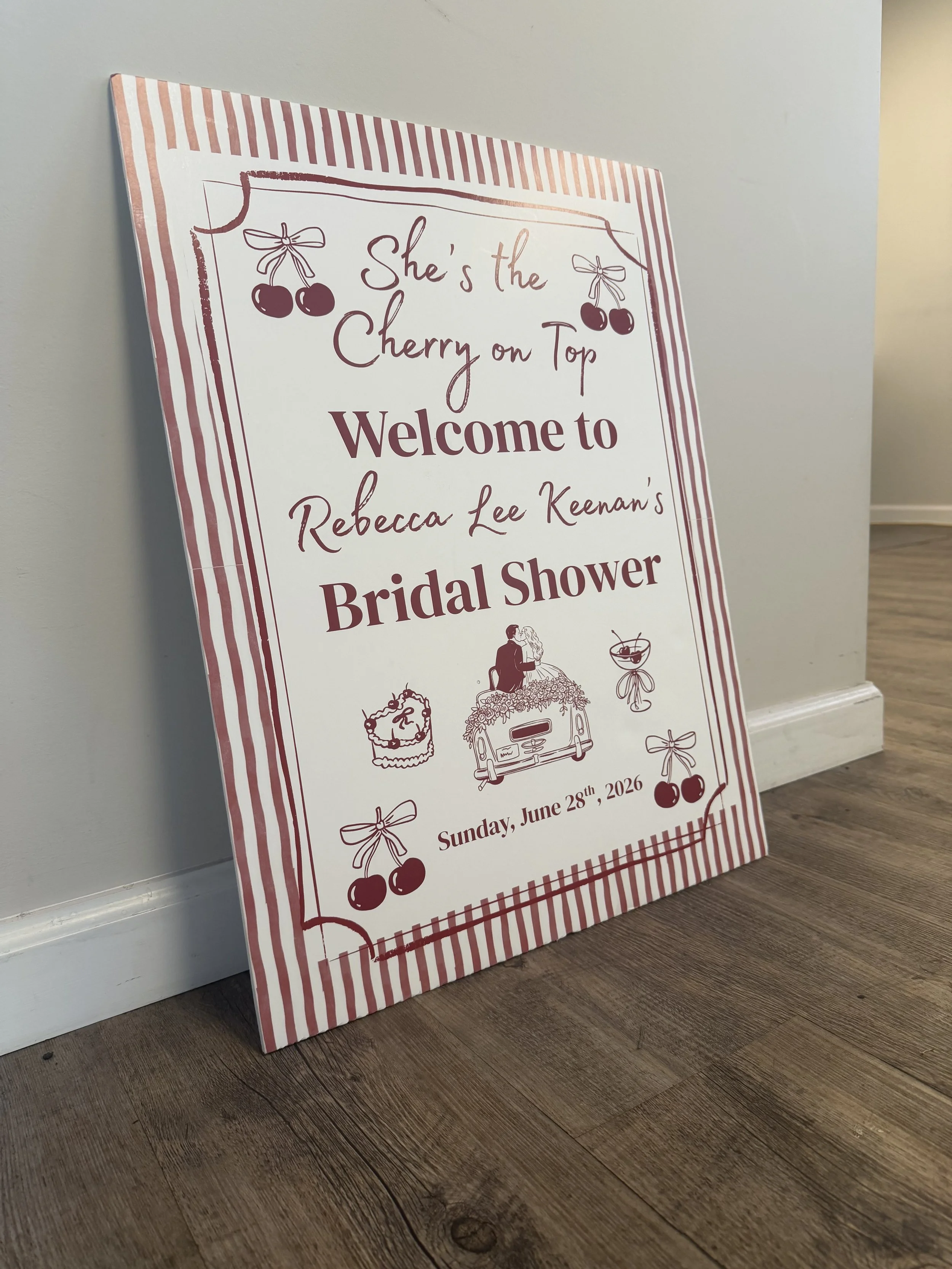 A welcome sign for a bridal shower, featuring cherries, a bride and groom, a cake, and a car, with red and white striped border.