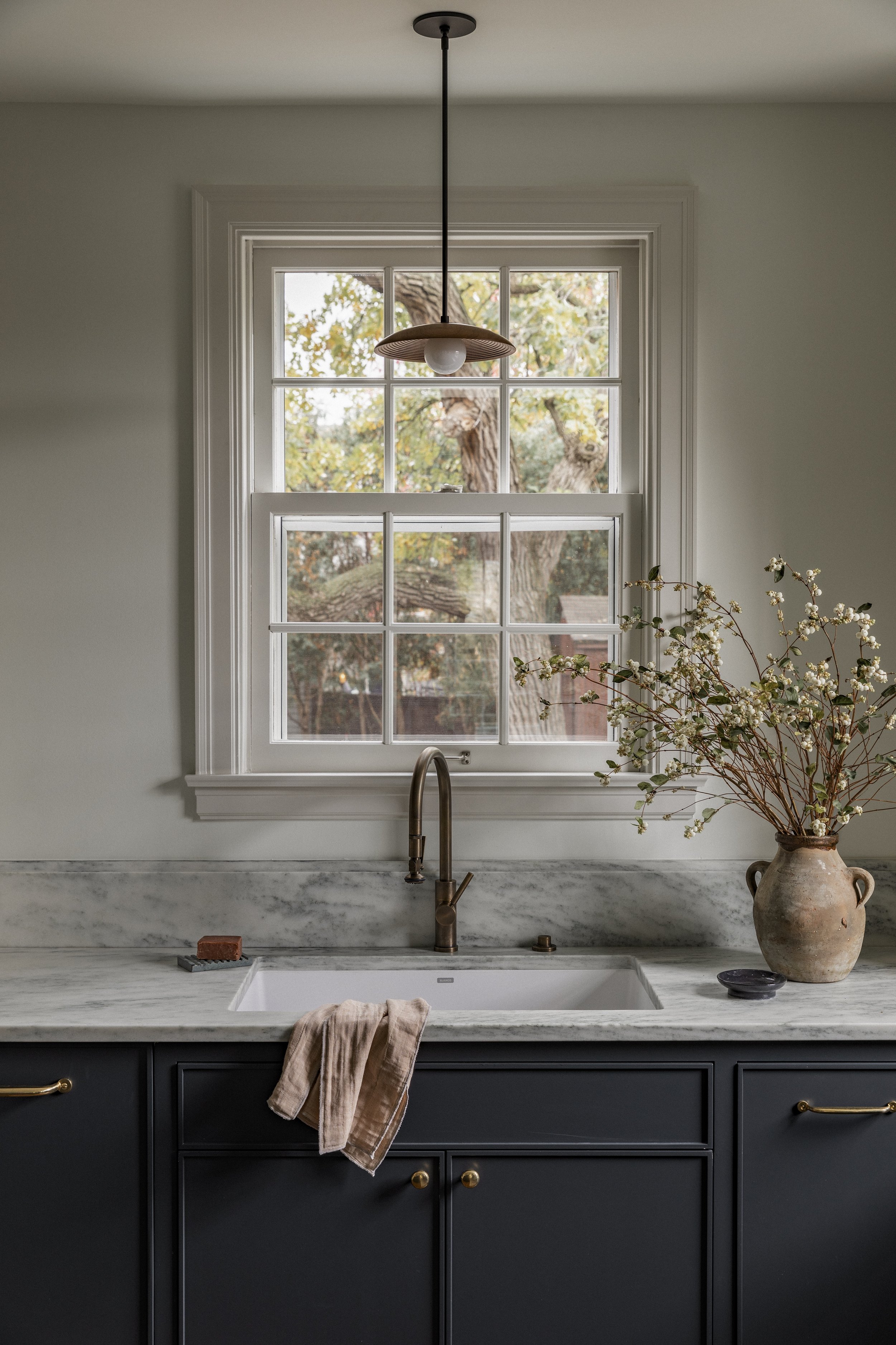 Kitchen sink and window detail in a Minneapolis remodel featuring marble countertops, an unlacquered brass faucet, and natural light.