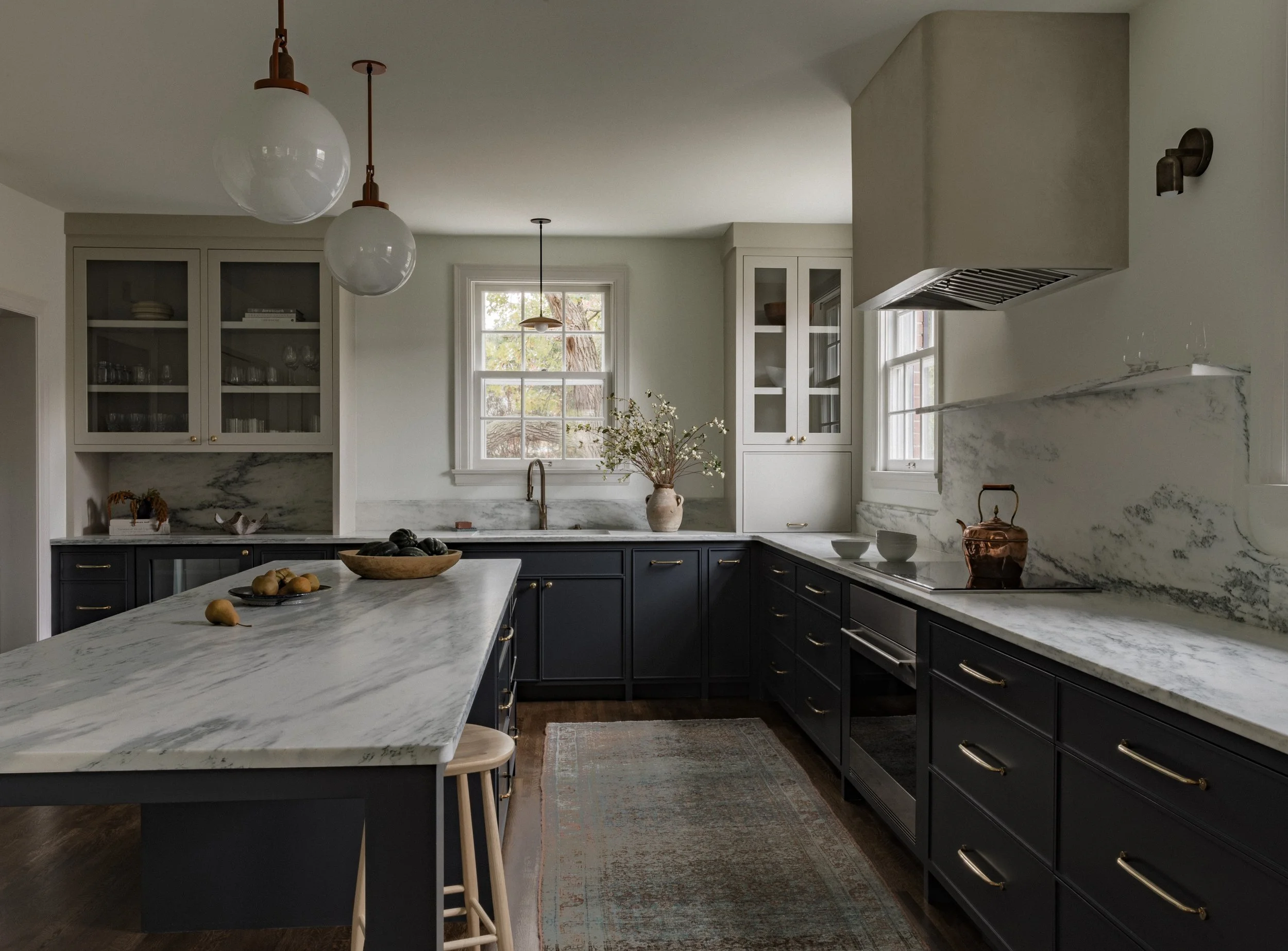 Transitional custom kitchen in a Minneapolis remodel featuring marble countertops, dark custom cabinetry, brass hardware, and a large island.