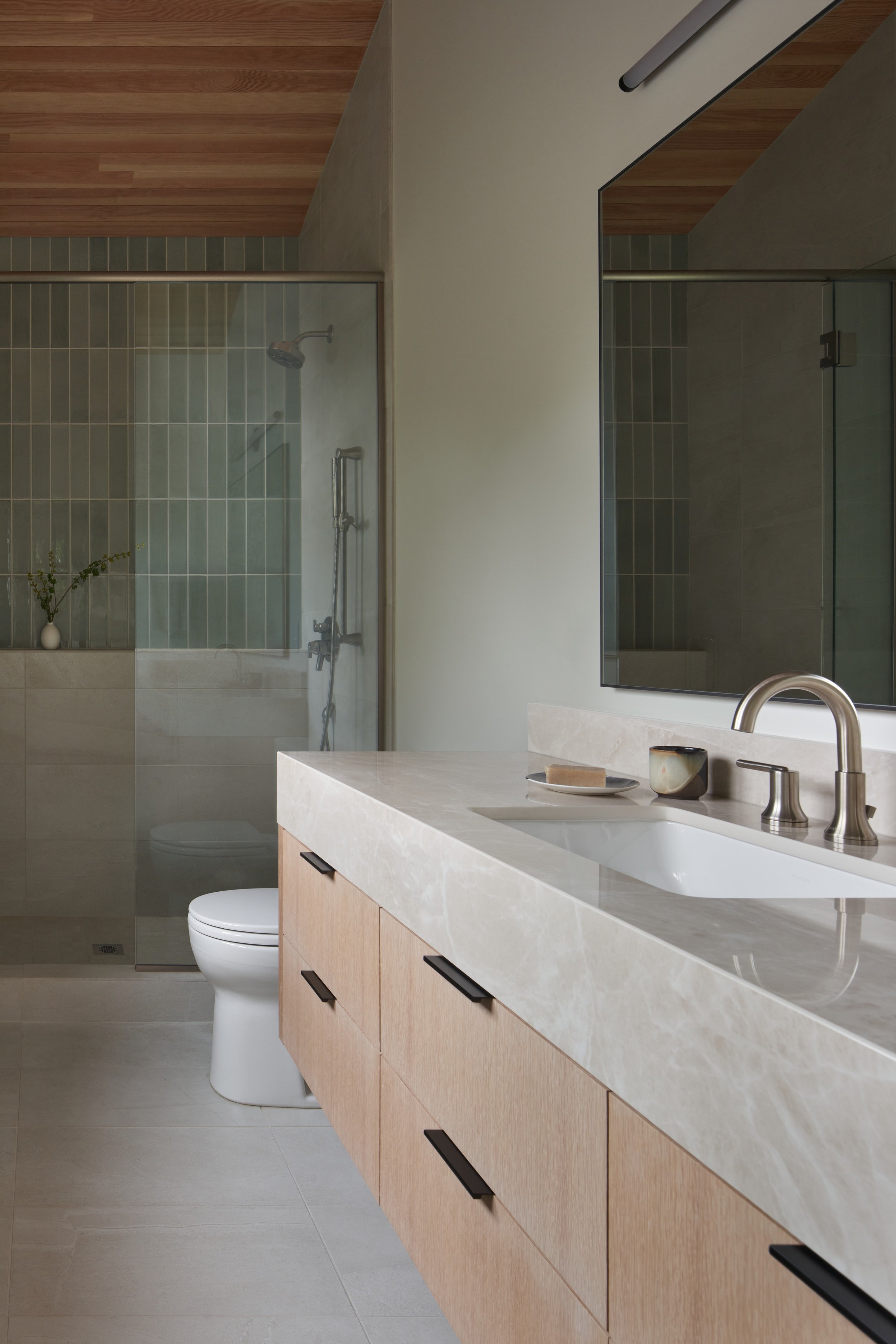 Primary bathroom with floating wood vanity, stone countertop, and walk-in shower at Parkway Heritage, a St. Paul home renovation by Karl Adalbert Architecture + Design.
