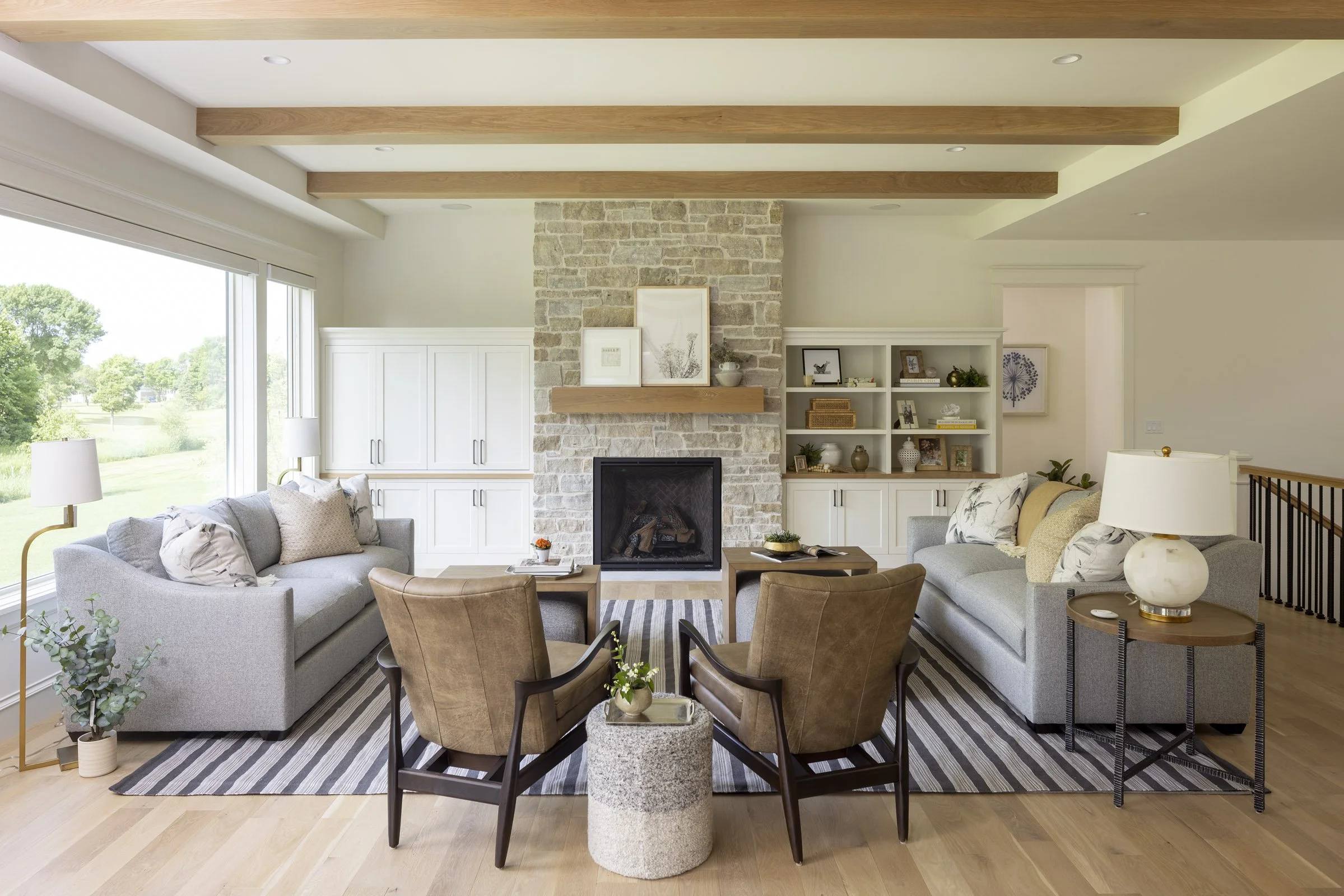 Living room in a Medina residence featuring a stone fireplace, custom built-ins, exposed wood beams, and expansive windows.