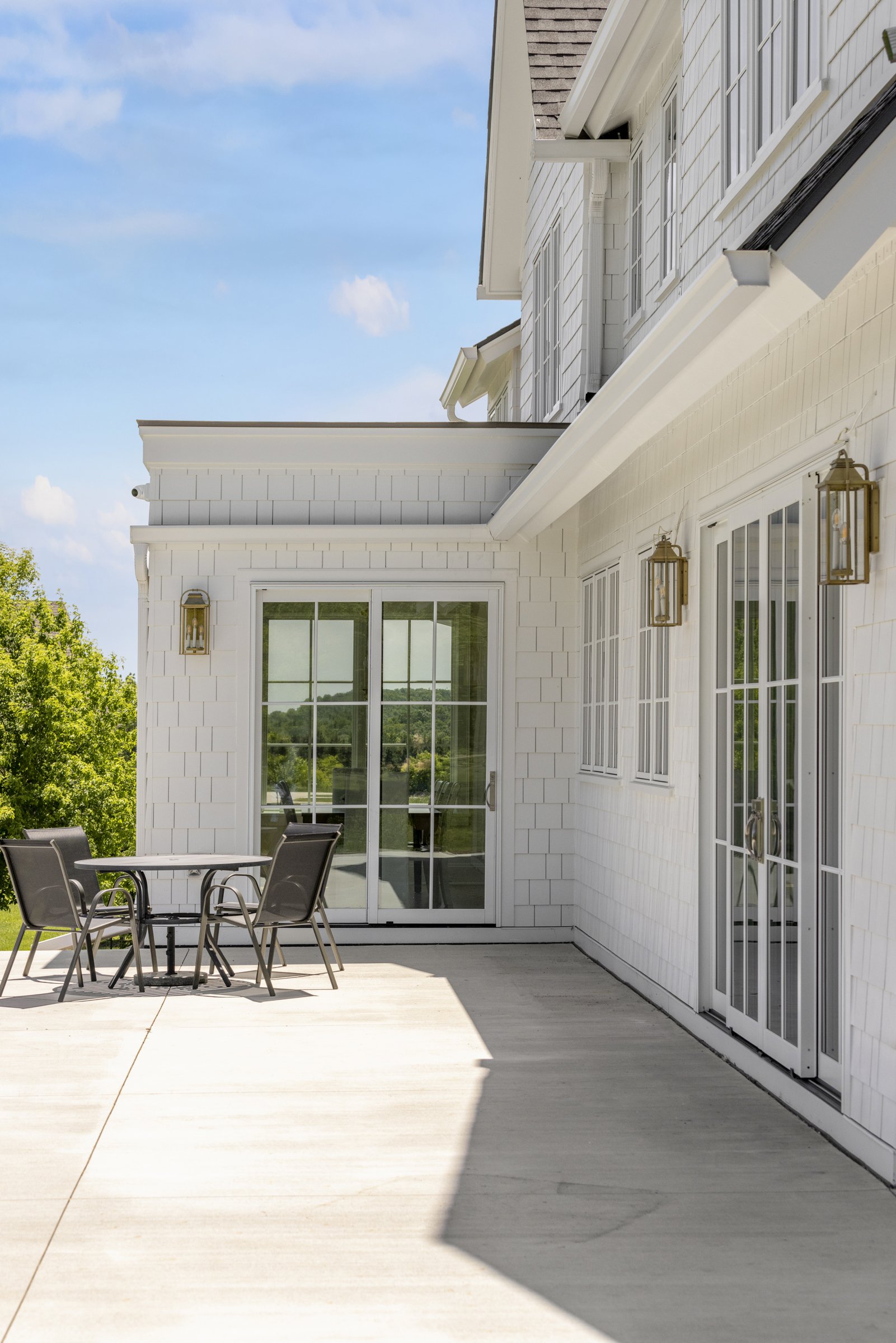 Covered backyard patio with outdoor seating and white farmhouse exterior.