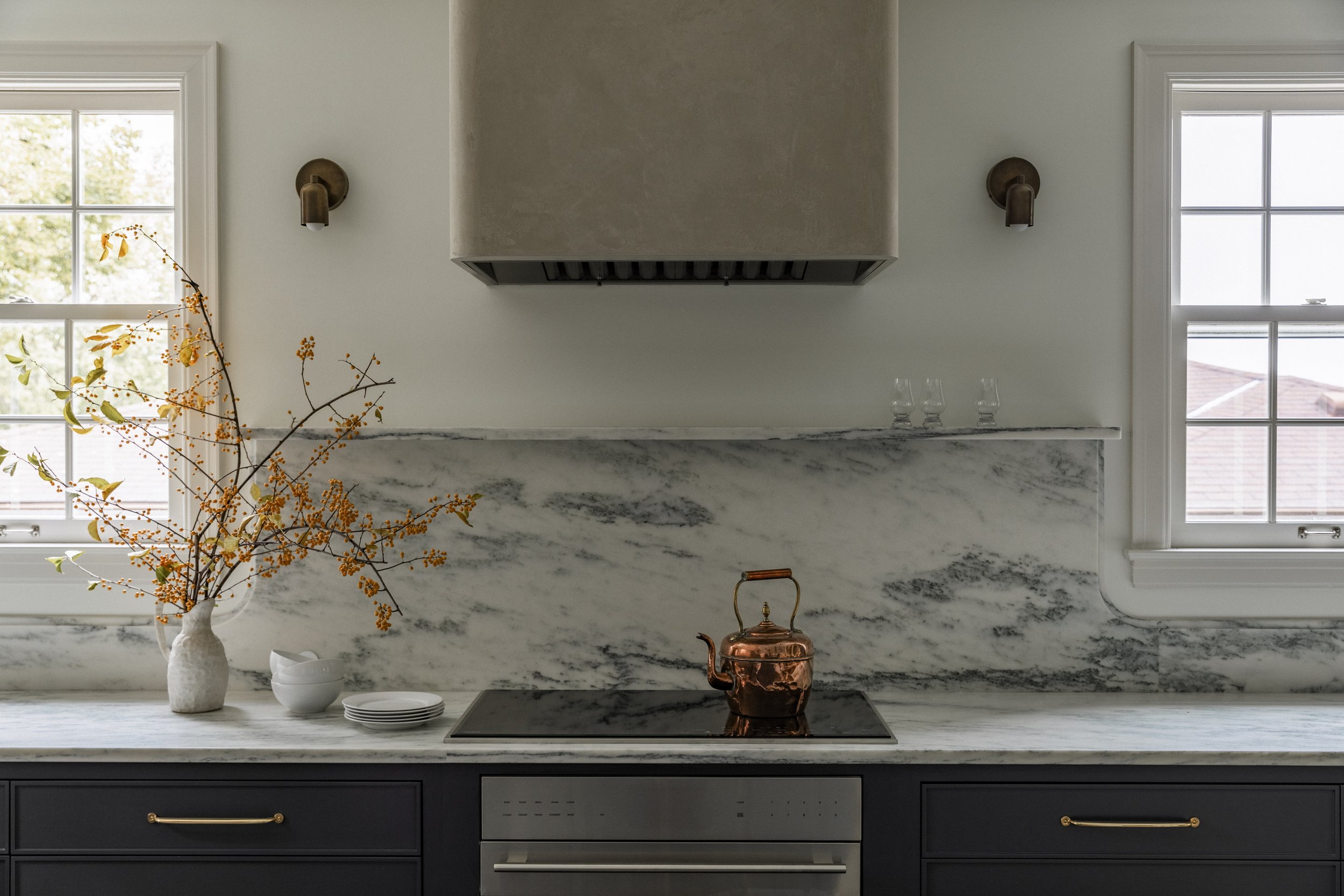 Custom kitchen cooktop wall in a Minneapolis remodel featuring a marble slab backsplash, plaster hood, and brass fixtures.