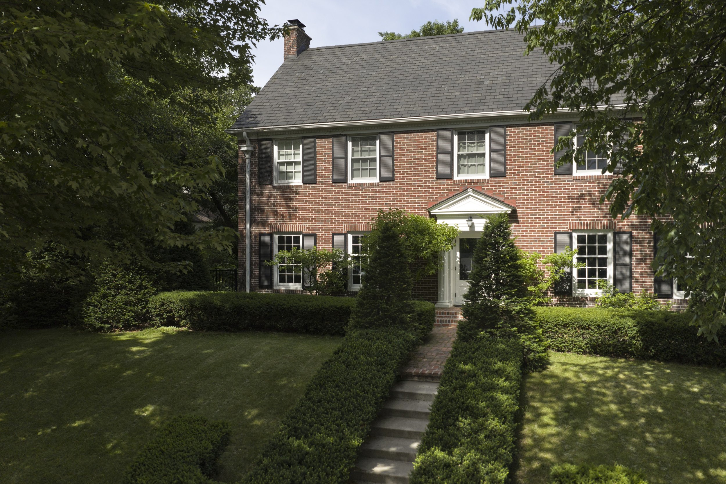 Front exterior of a renovated traditional brick home in Minneapolis featuring symmetrical architecture, mature landscaping, and a formal entry.