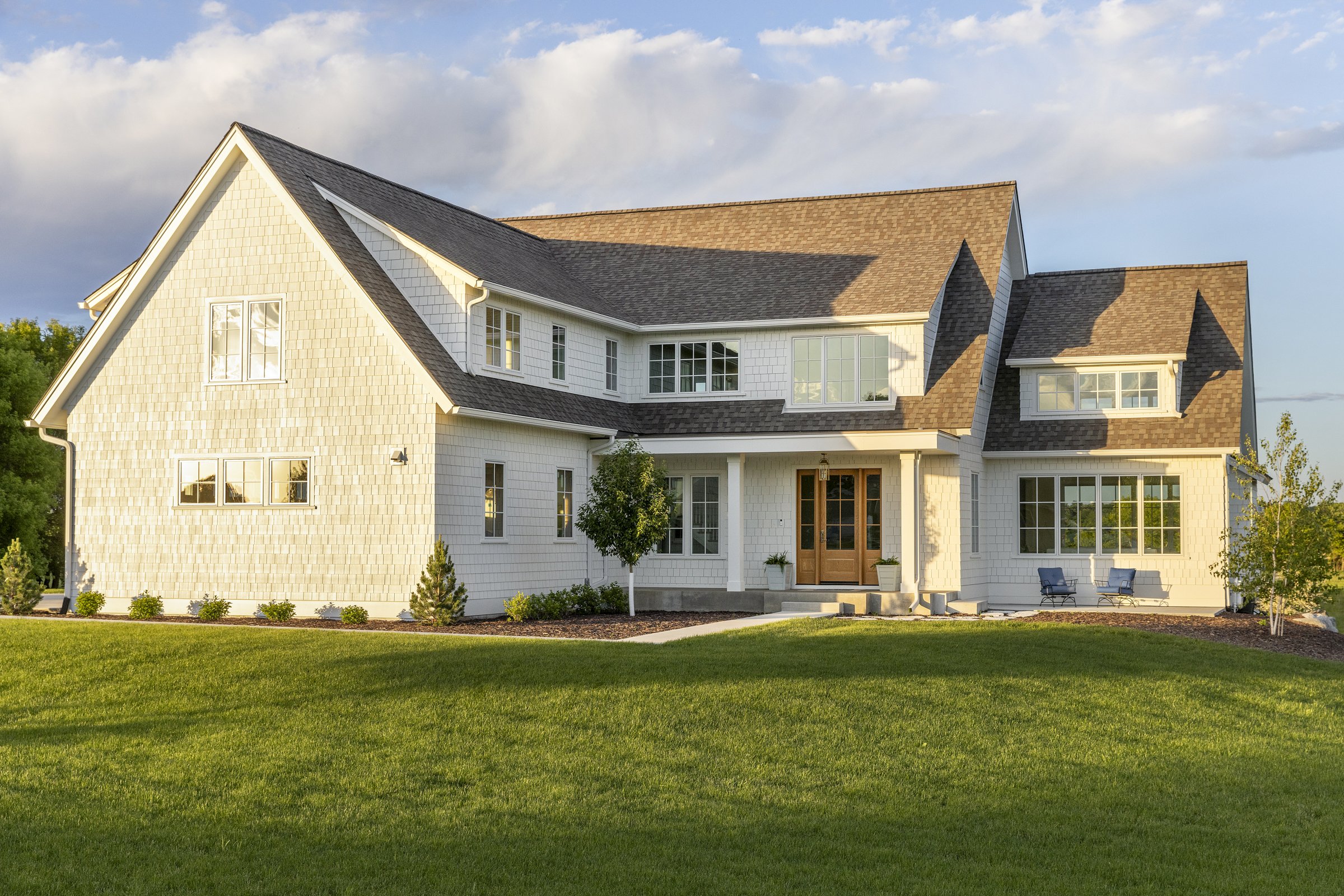 Front elevation of a white modern farmhouse with shake siding and expansive front lawn.