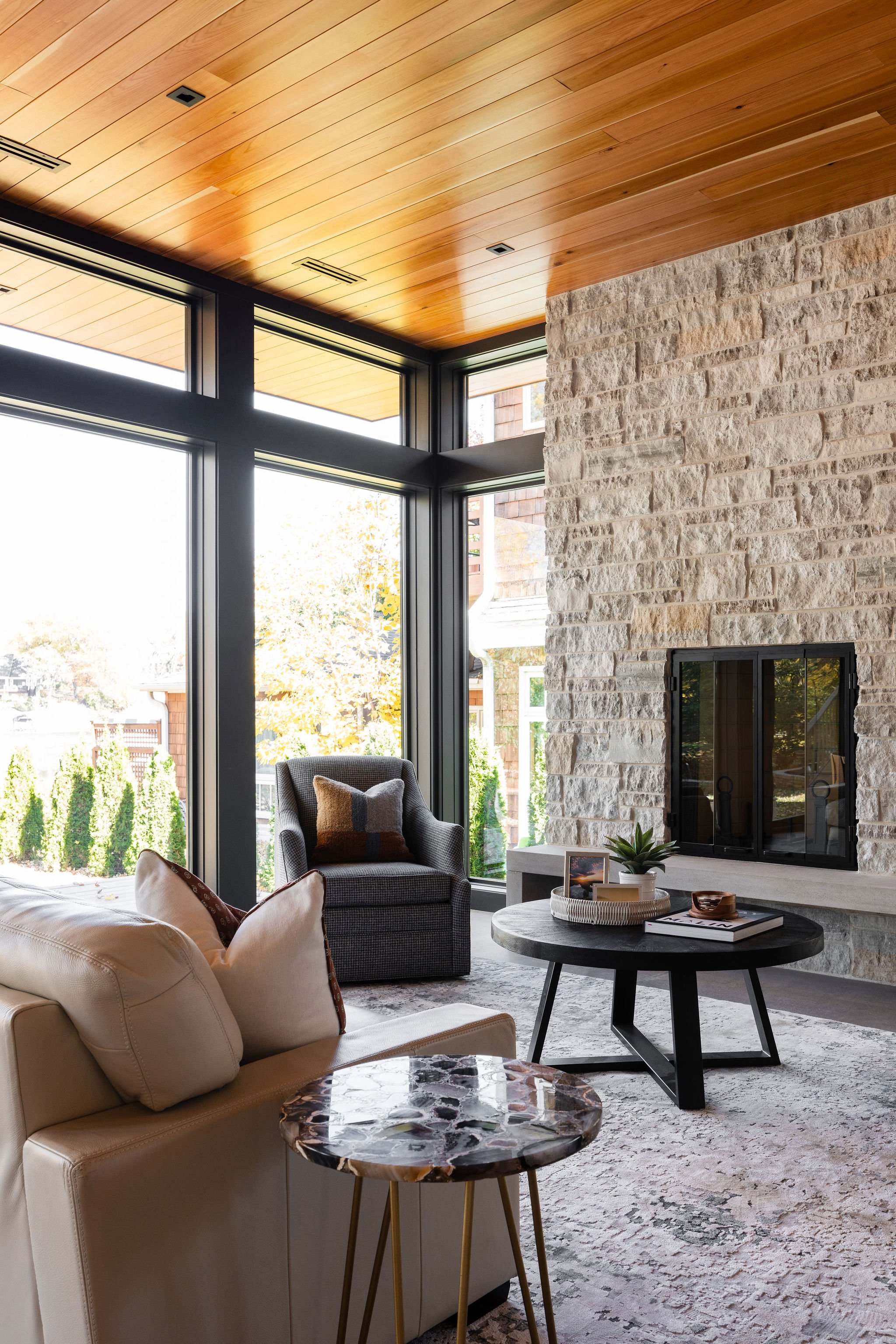 Modern living room with floor-to-ceiling windows, limestone fireplace, and cedar ceiling.