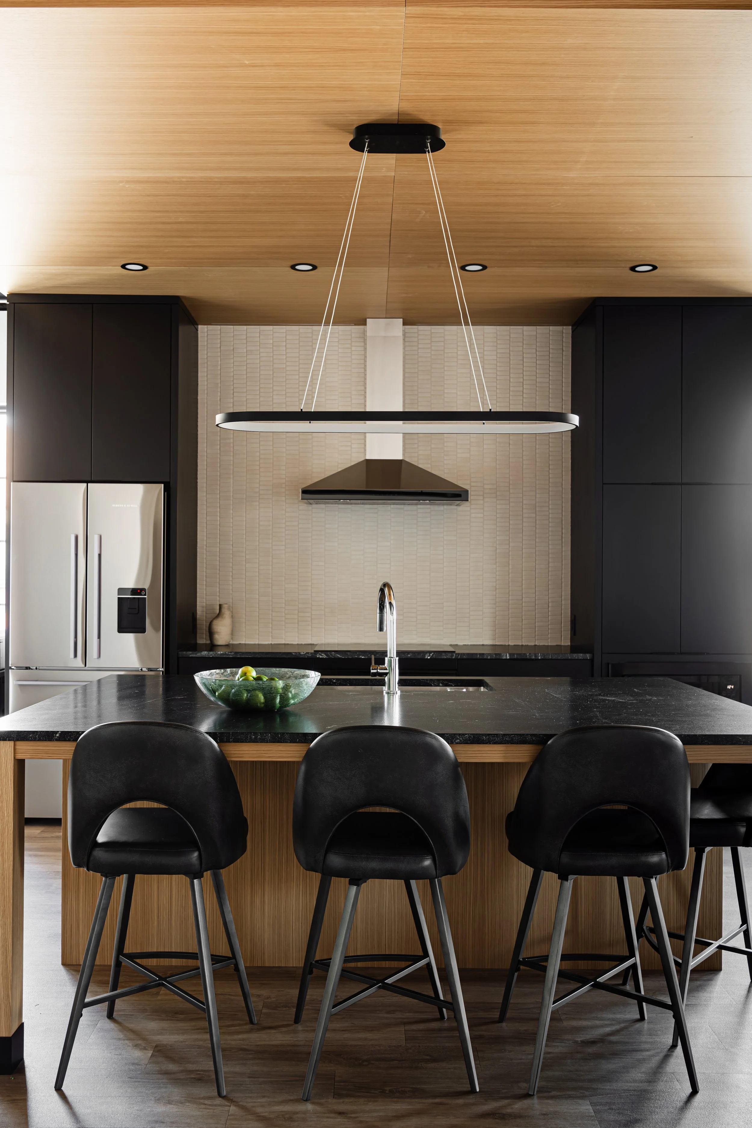 Modern kitchen with oversized island, wood ceiling feature, and black cabinetry in a luxury auto condo in Medina, Minnesota.