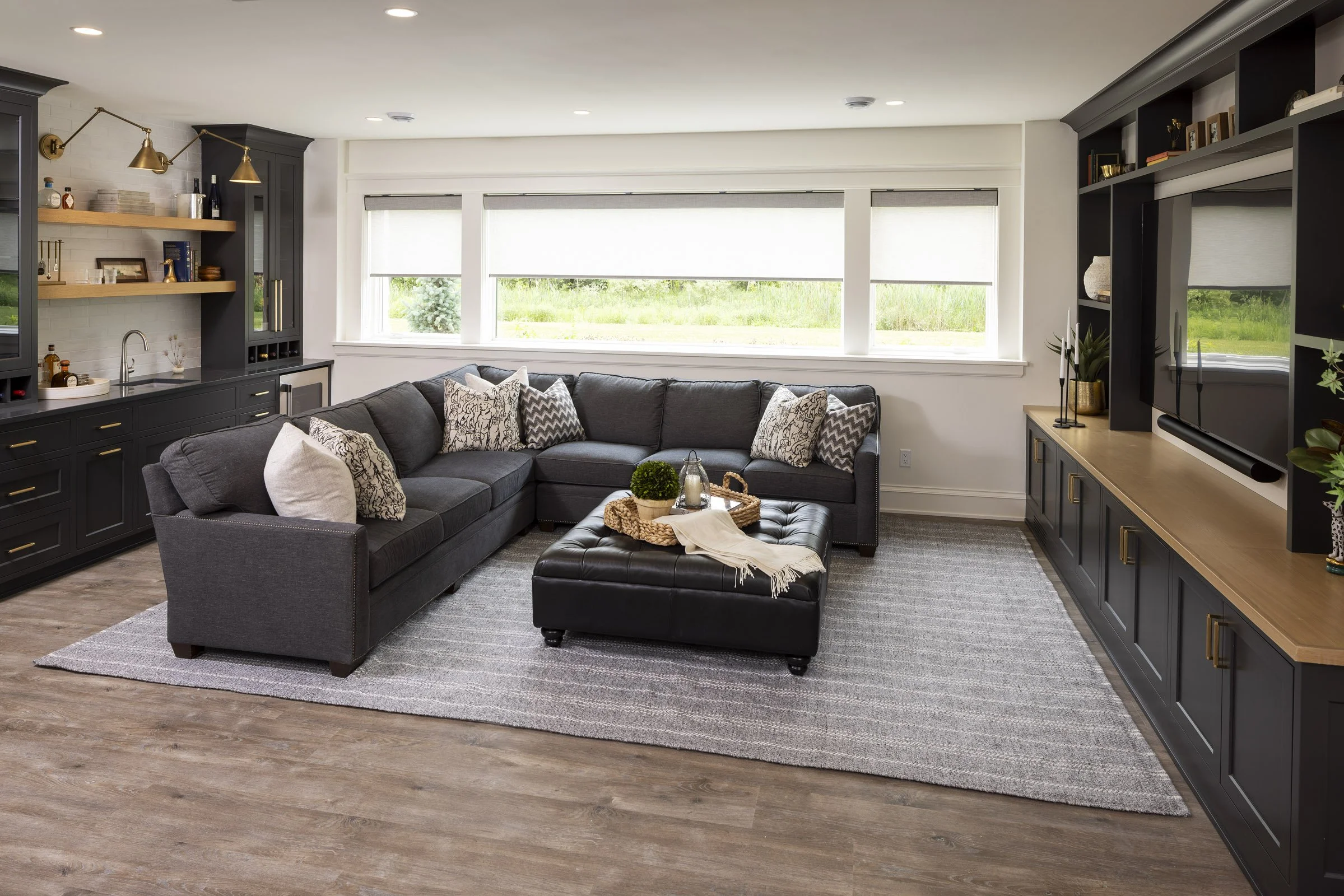 Lower-level family room in a Medina custom home featuring dark built-ins, a media wall, wet bar, and gathering space.