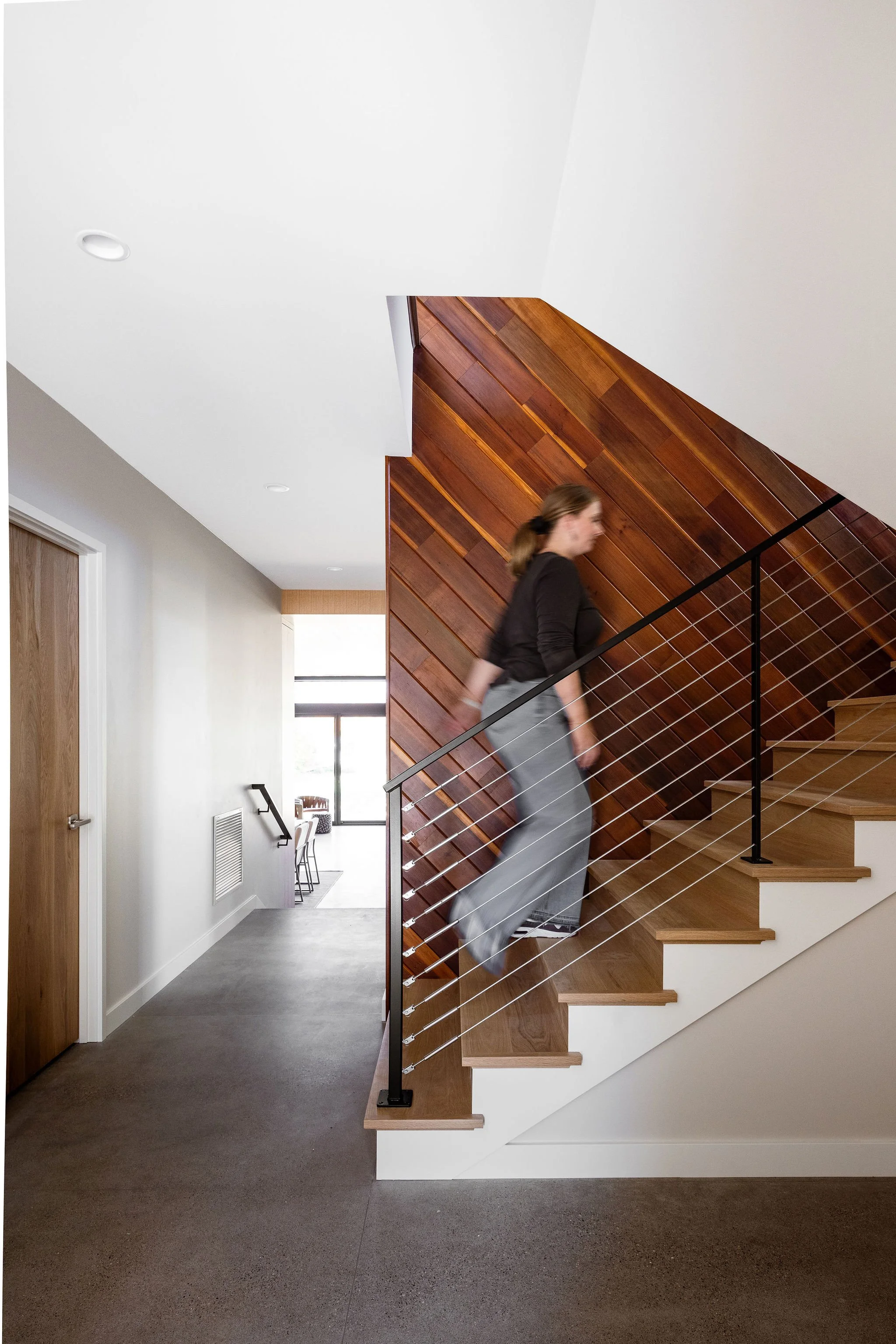 Modern staircase with cable railing, wood feature wall, and polished concrete flooring.