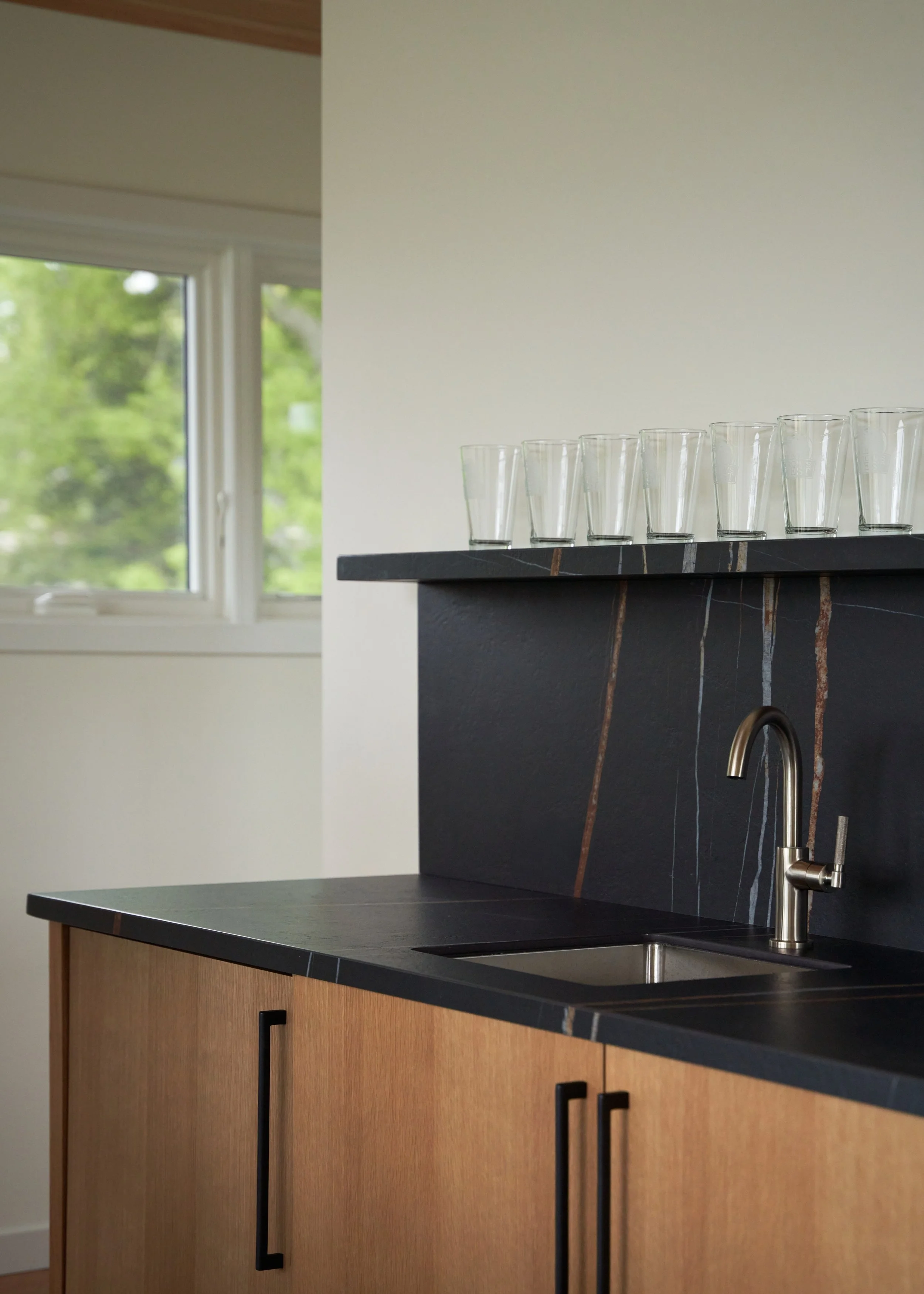 Custom wet bar with wood cabinetry, black stone countertop, and architectural detailing at Parkway Heritage, a St. Paul home renovation by Karl Adalbert Architecture + Design.