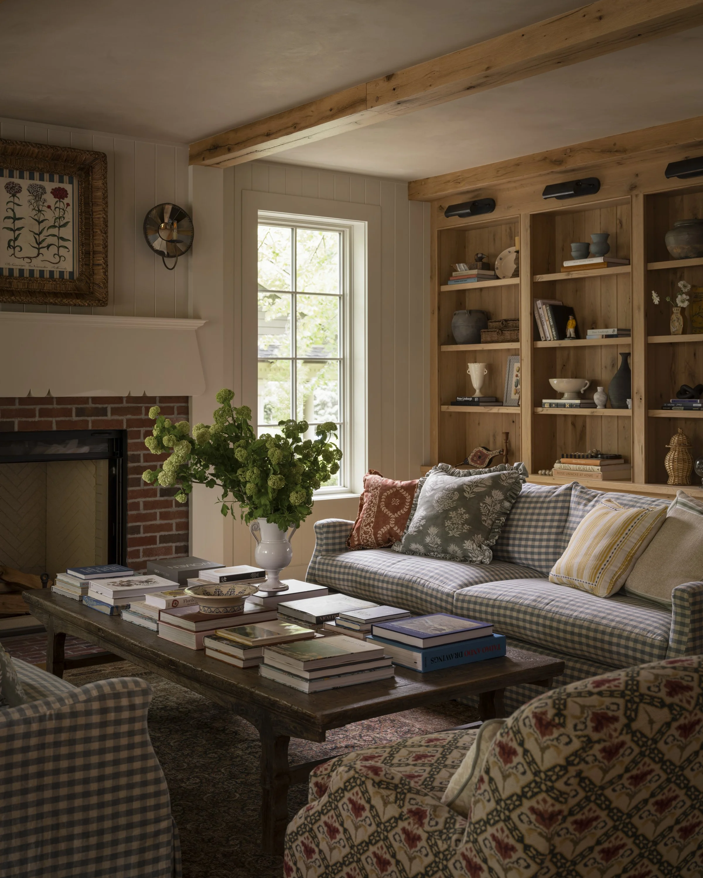 Cozy family room in a Cottagewood custom home with reclaimed wood beams, built-in oak shelving, brick fireplace, and layered traditional furnishings.