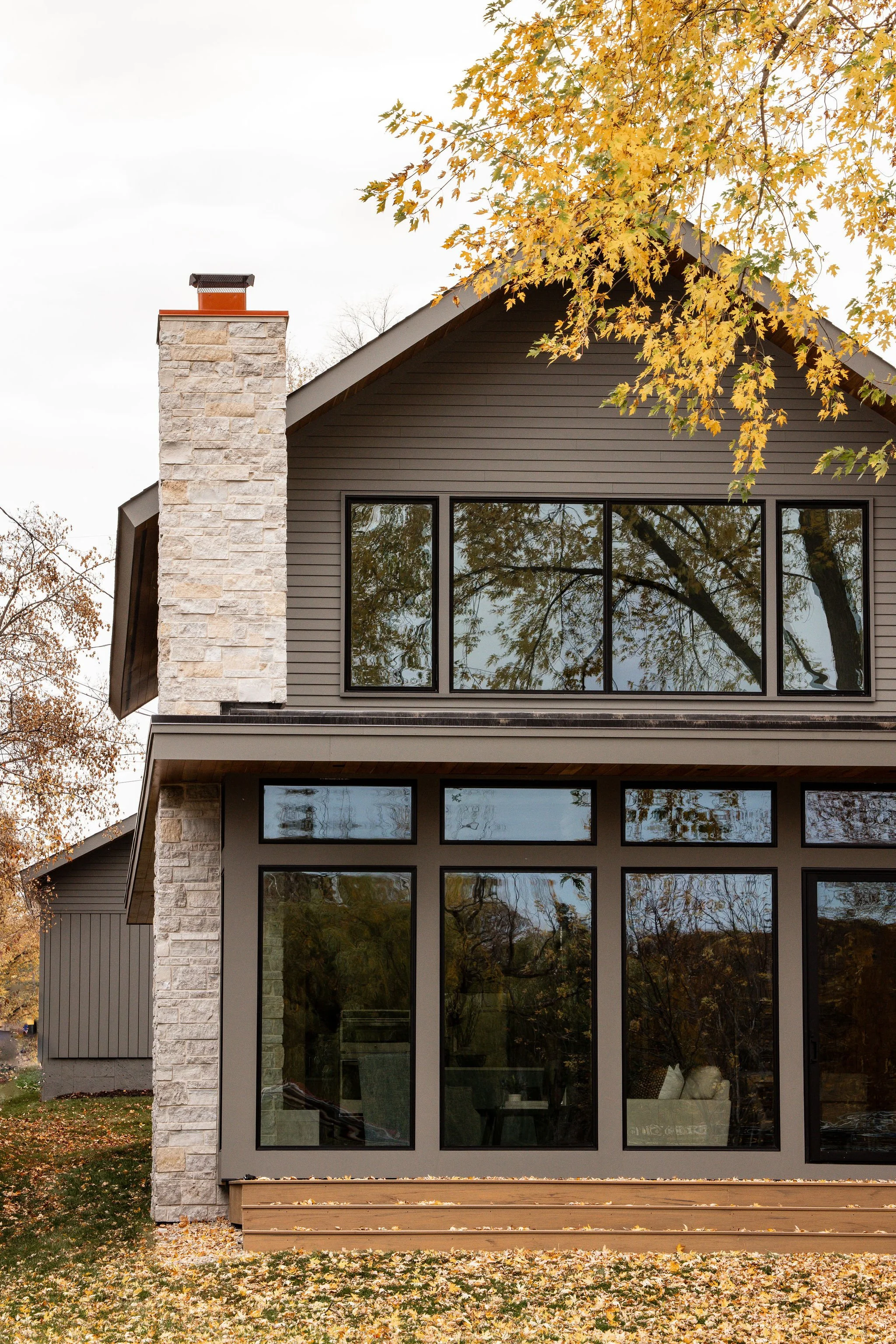 Modern Lake Minnetonka residence featuring expansive glazing, stone chimney, and contemporary architectural detailing.