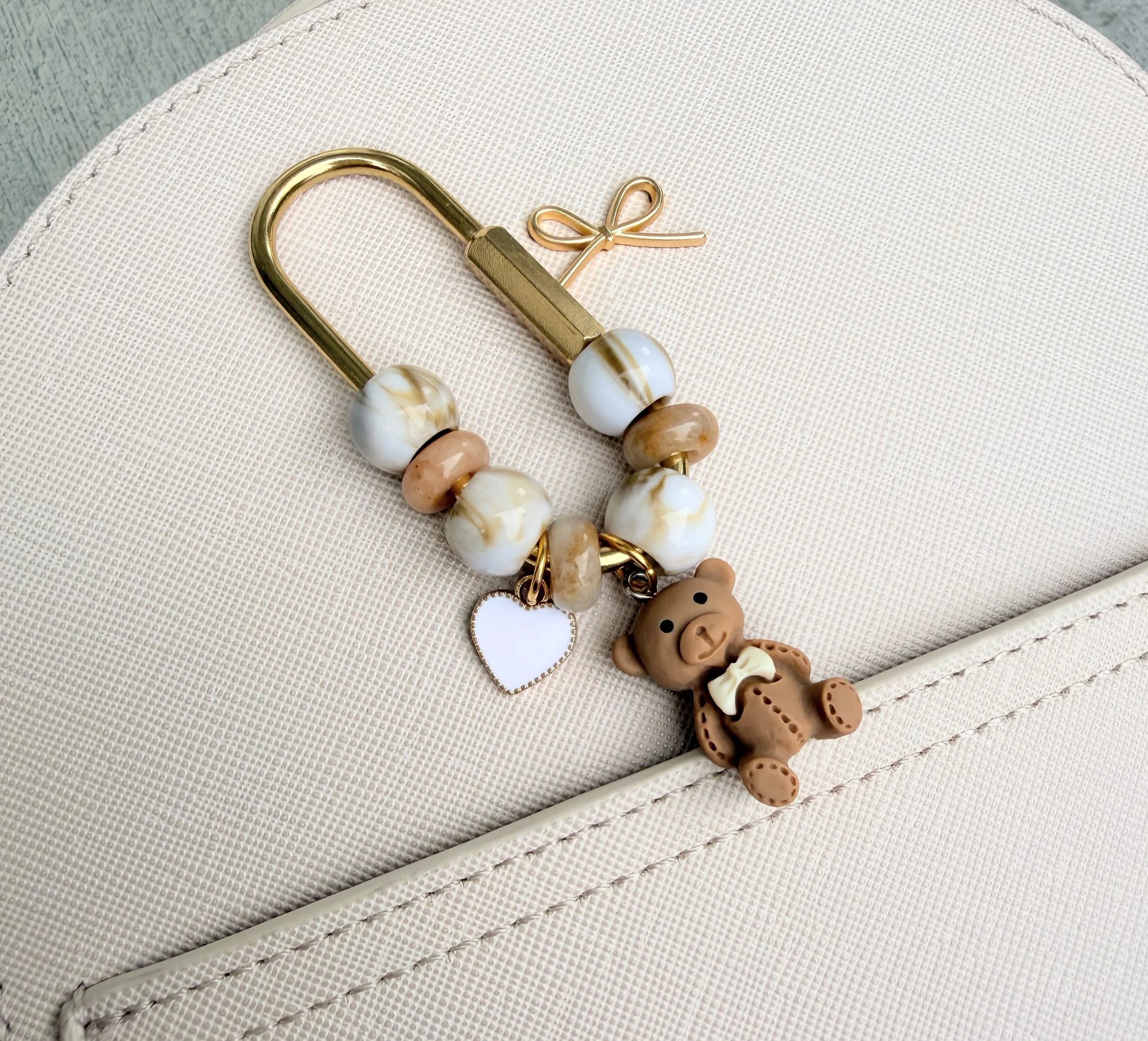 Close-up of a handmade jewelry piece with pearls, beads, and a small bear-shaped charm on a beige fabric surface.