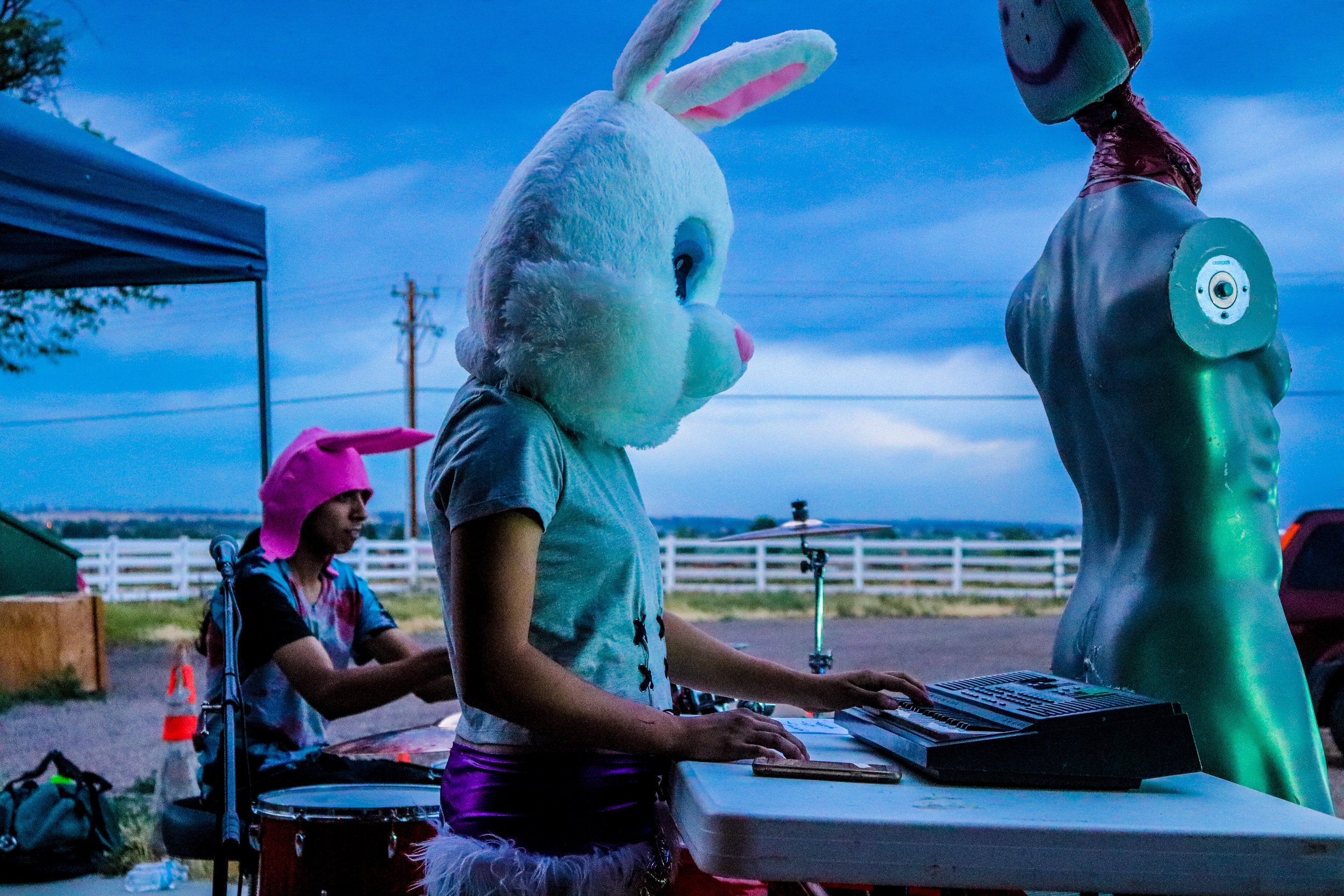 People dressed in Easter bunny costumes, with one playing a keyboard and another wearing a pink hat, performing outdoors during twilight.