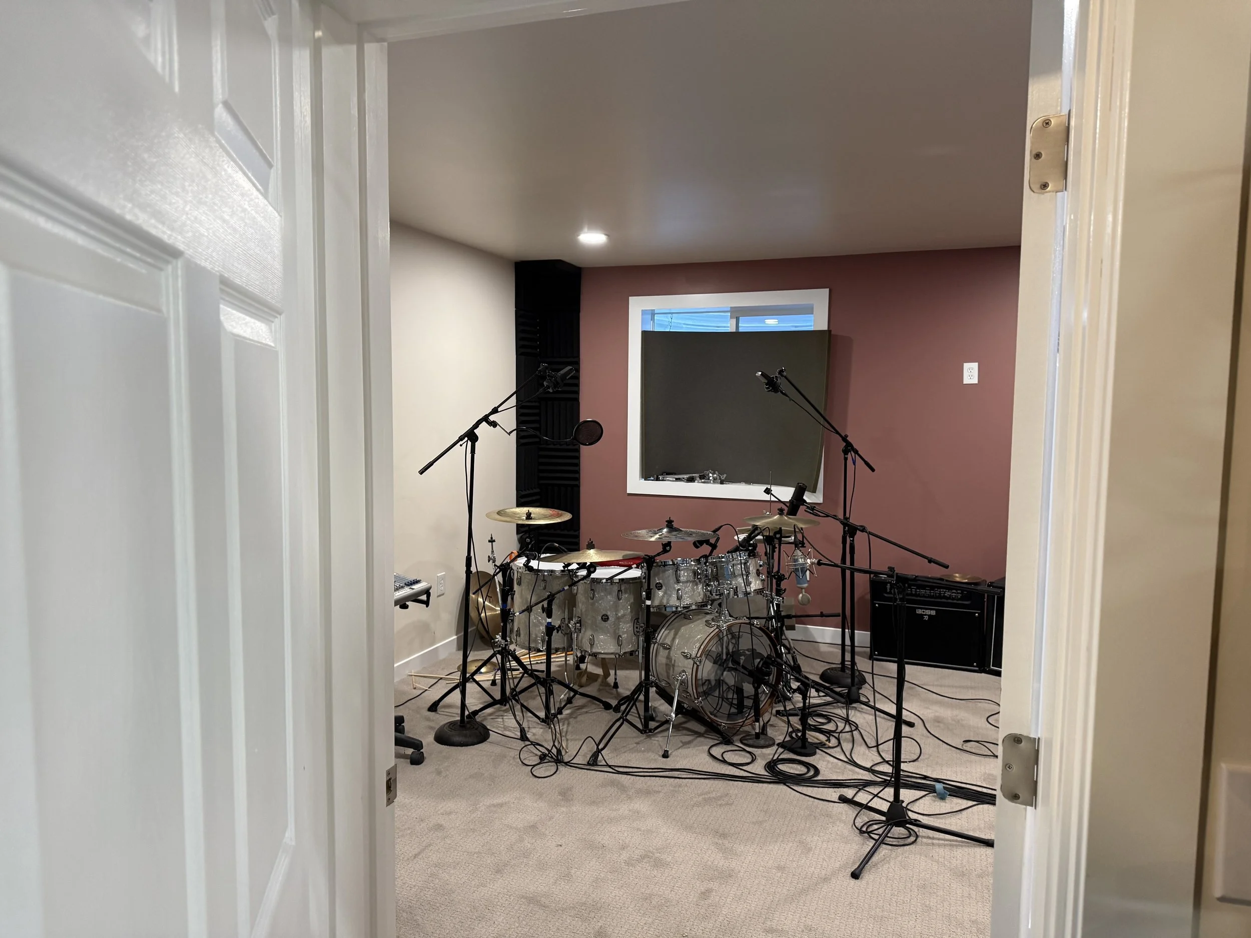 Music studio room with a drum set, microphones, speakers, and soundproofing panels.